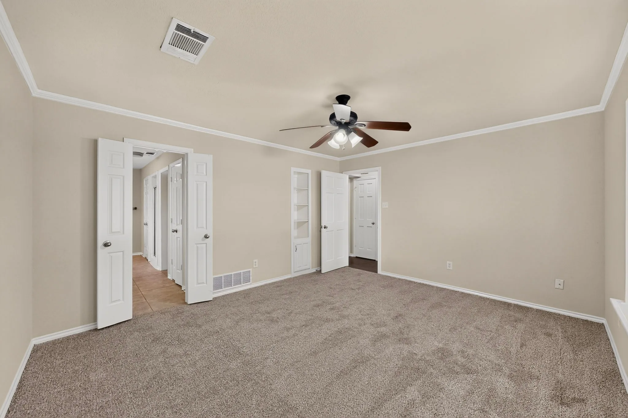 Spacious carpeted room featuring a ceiling fan, crown molding, and built-in shelving