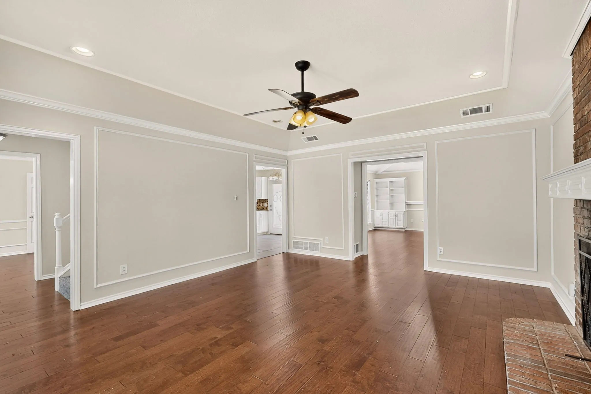 Spacious interior featuring wood-finish flooring, a tray ceiling with recessed lighting, an overhead ceiling fan, and intricate wall paneling
