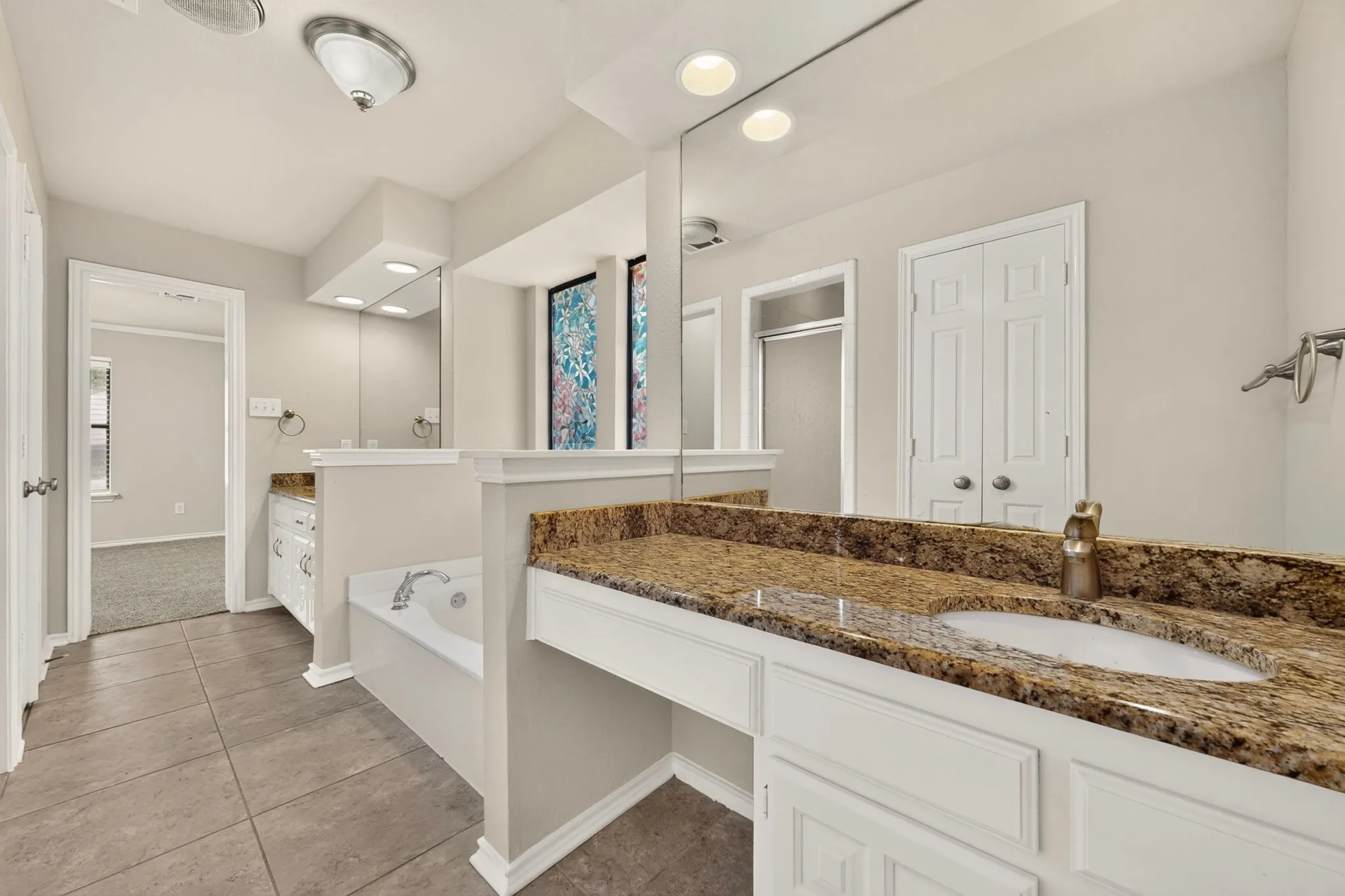 Spacious bathroom featuring dual vanity counters with stone surfaces, an integrated soaking tub, tiled flooring, and a separate glass-enclosed shower