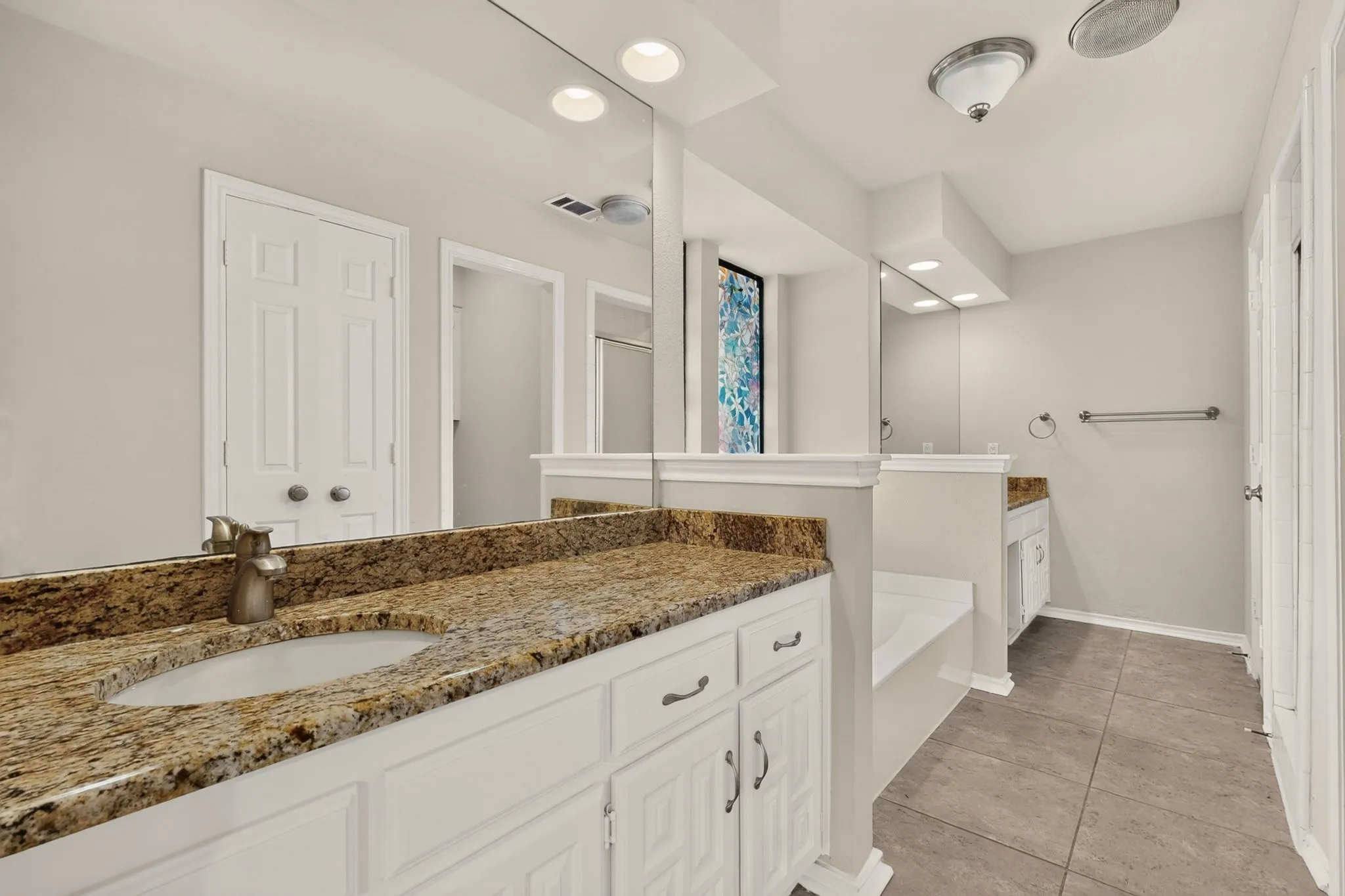 Bathroom featuring dual vanities with granite countertops, integrated sinks, white cabinetry, and full-wall mirrors