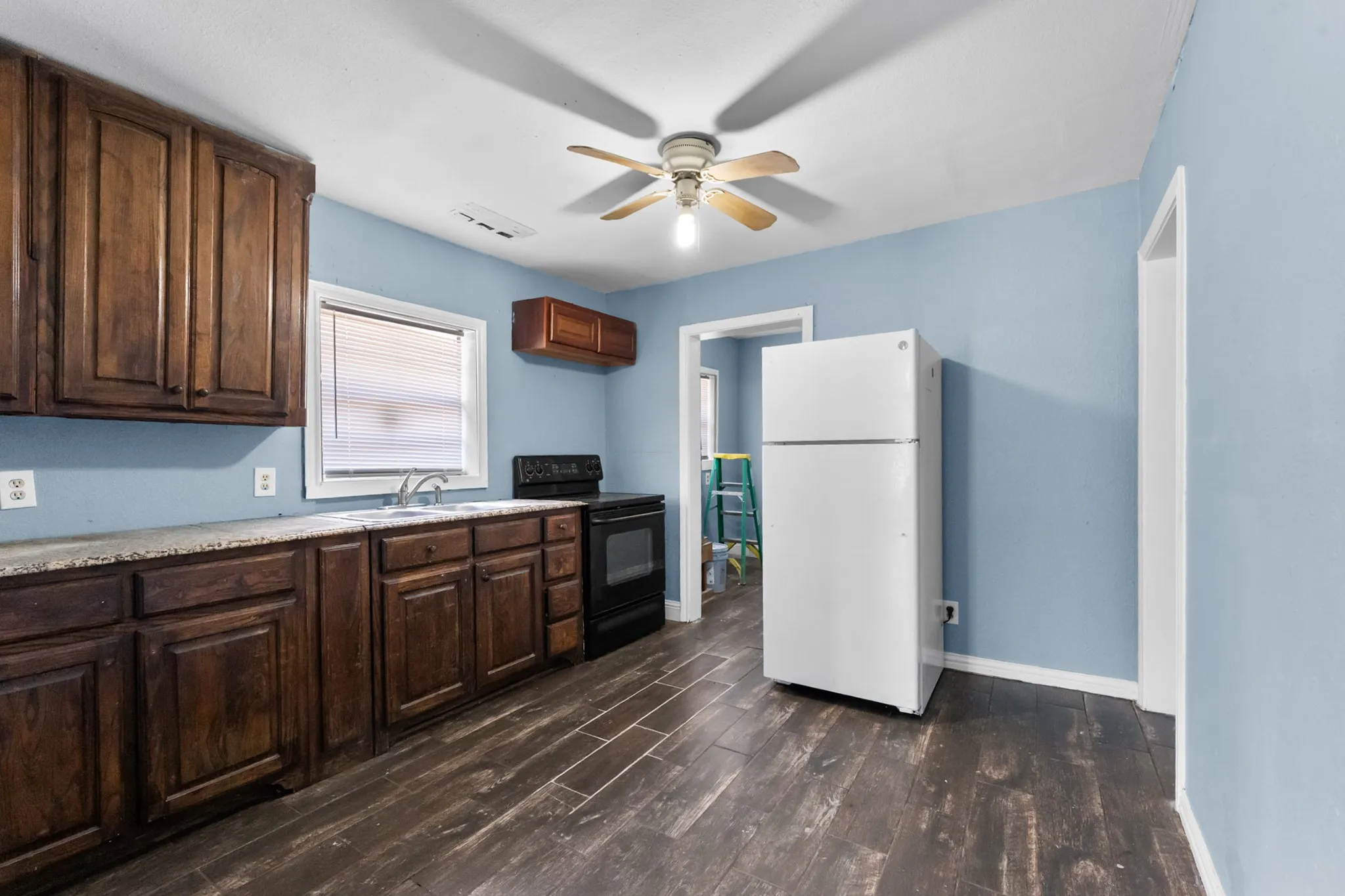 Kitchen featuring wood-finish flooring, wood cabinetry, stone-finish countertops, and a ceiling fan with integrated lighting