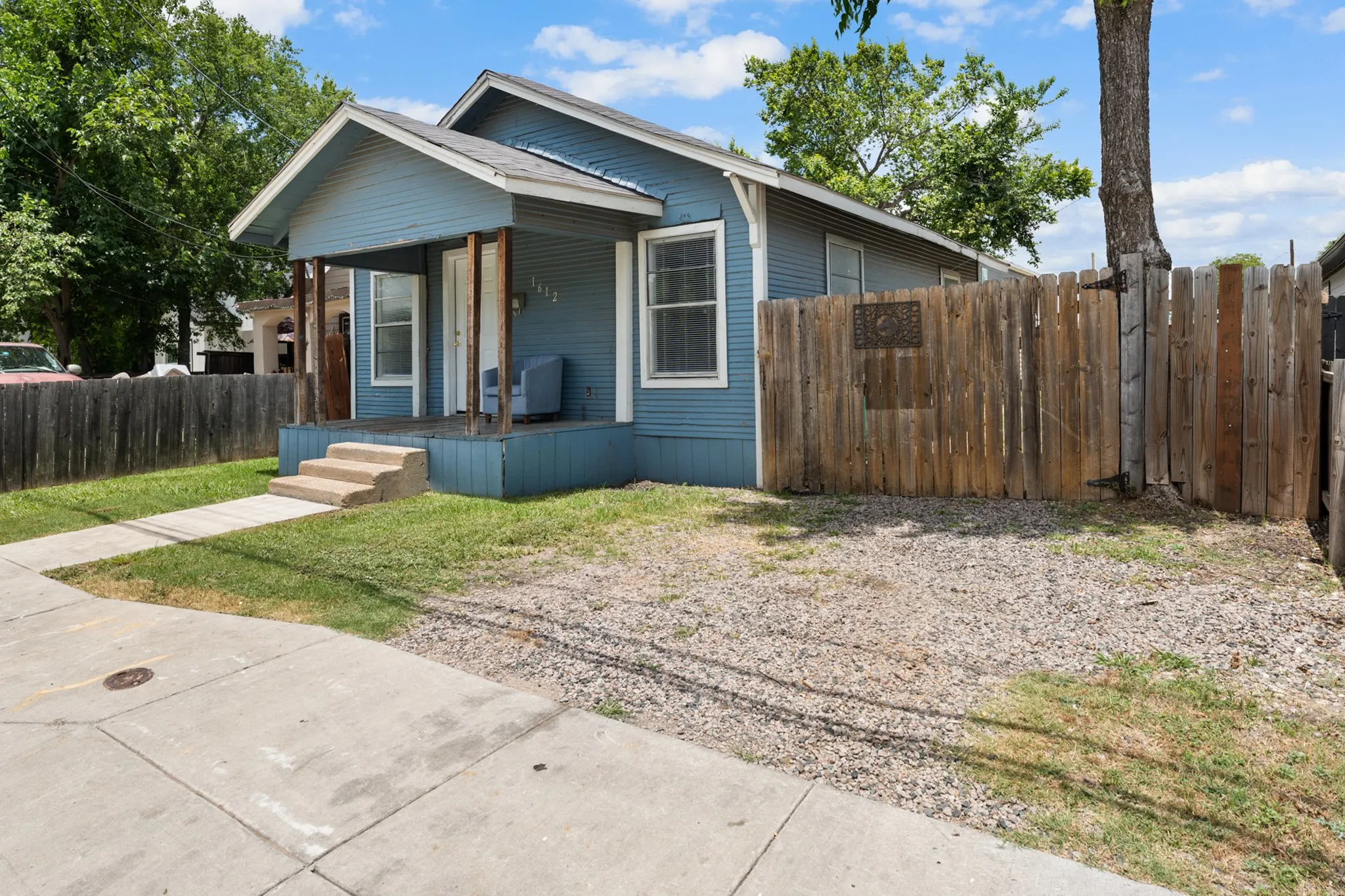Blue siding exterior with a covered front porch, concrete steps, and a partial privacy fence