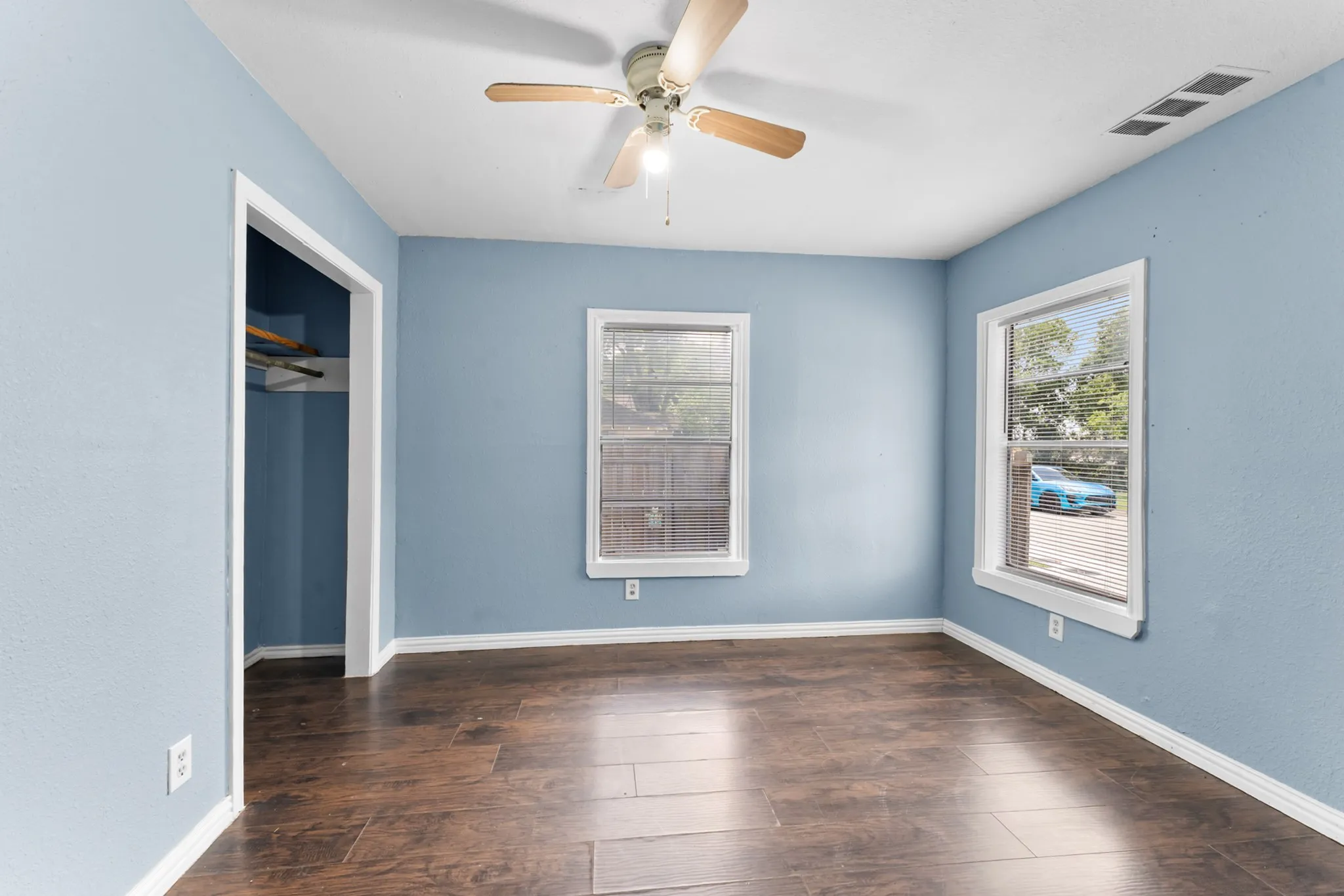 Wood-finish flooring, light blue walls, two windows, and a ceiling fan