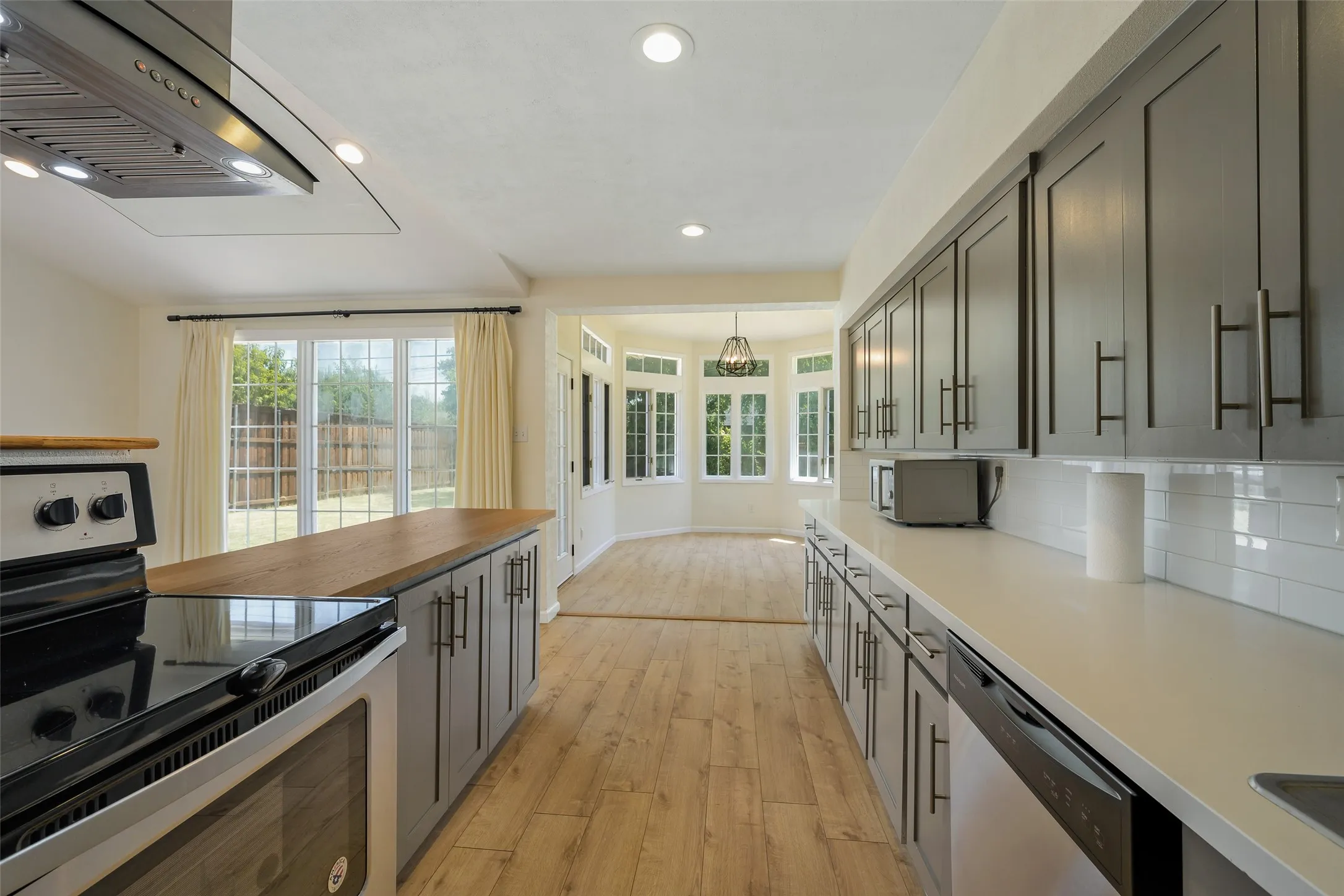 Kitchen featuring a wood-finish island countertop, recessed lighting, stainless steel range hood, light-toned wood-finish flooring, and a subway tile backsplash
