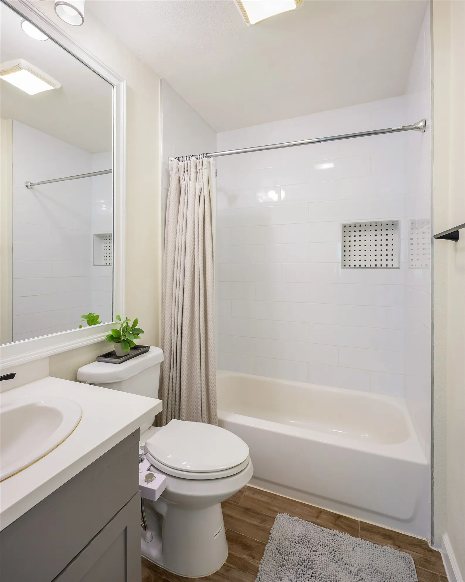 Full bathroom featuring a white vanity with a rectangular sink, wood-finish flooring, a toilet, and a bathtub with white subway tile surround and a recessed niche