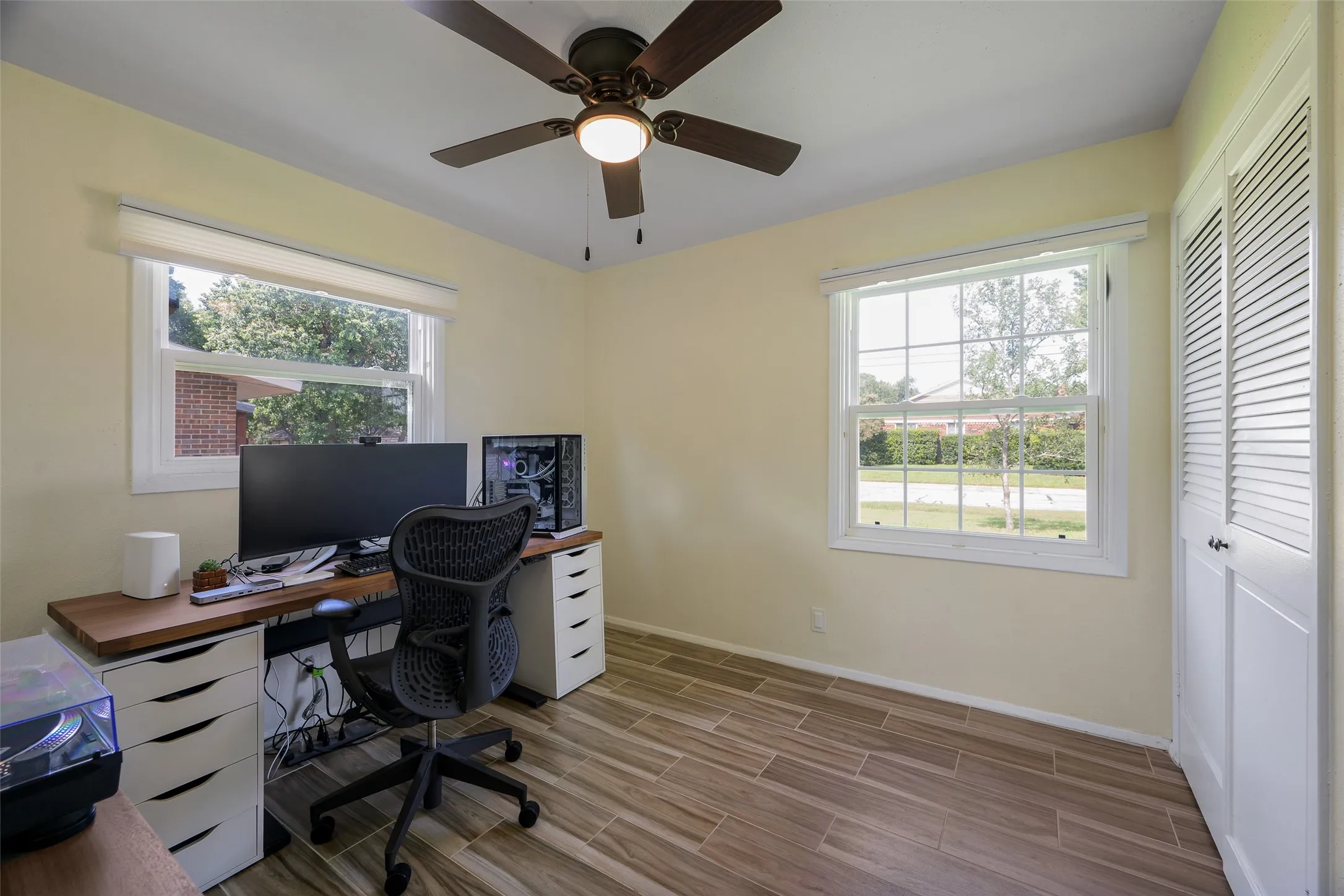 Room featuring wood-finish tile flooring, two white-framed windows, and a ceiling fan with integrated lighting