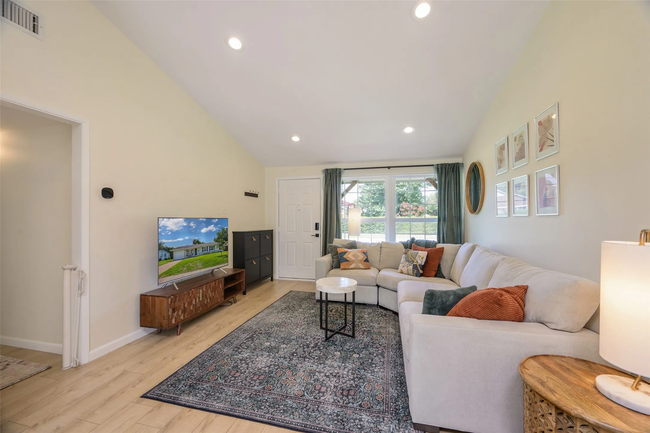 Living area featuring wood-finish flooring, vaulted ceilings, recessed lighting, and a large window with exterior views