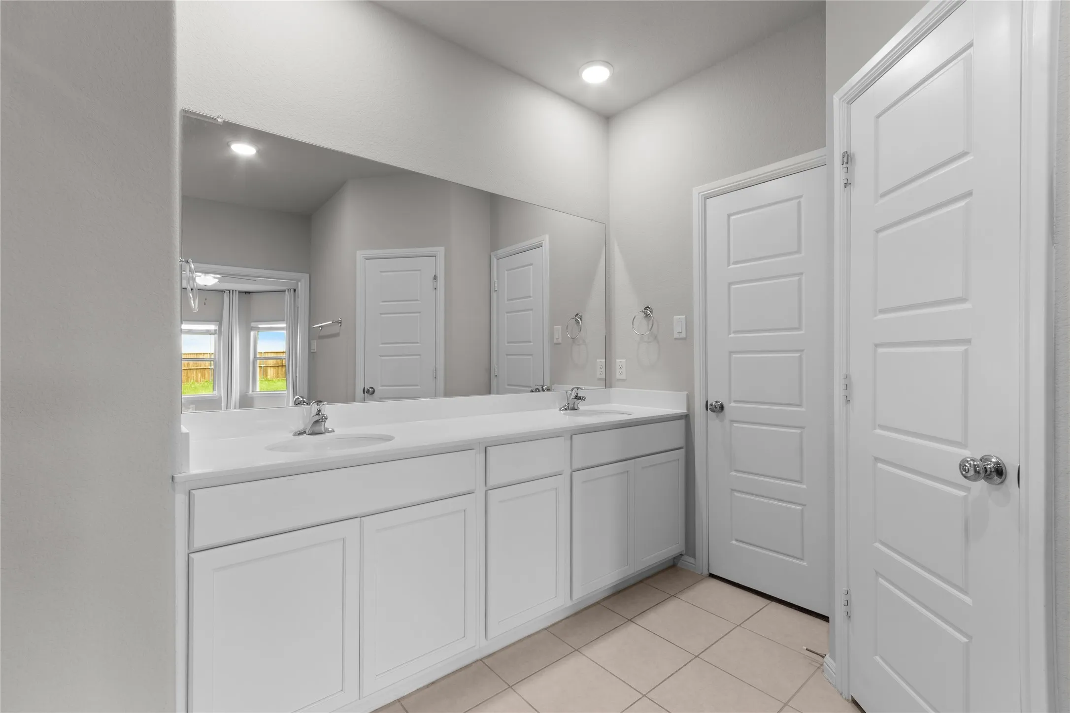 White vanity with dual sinks, a continuous mirror, and recessed lighting
