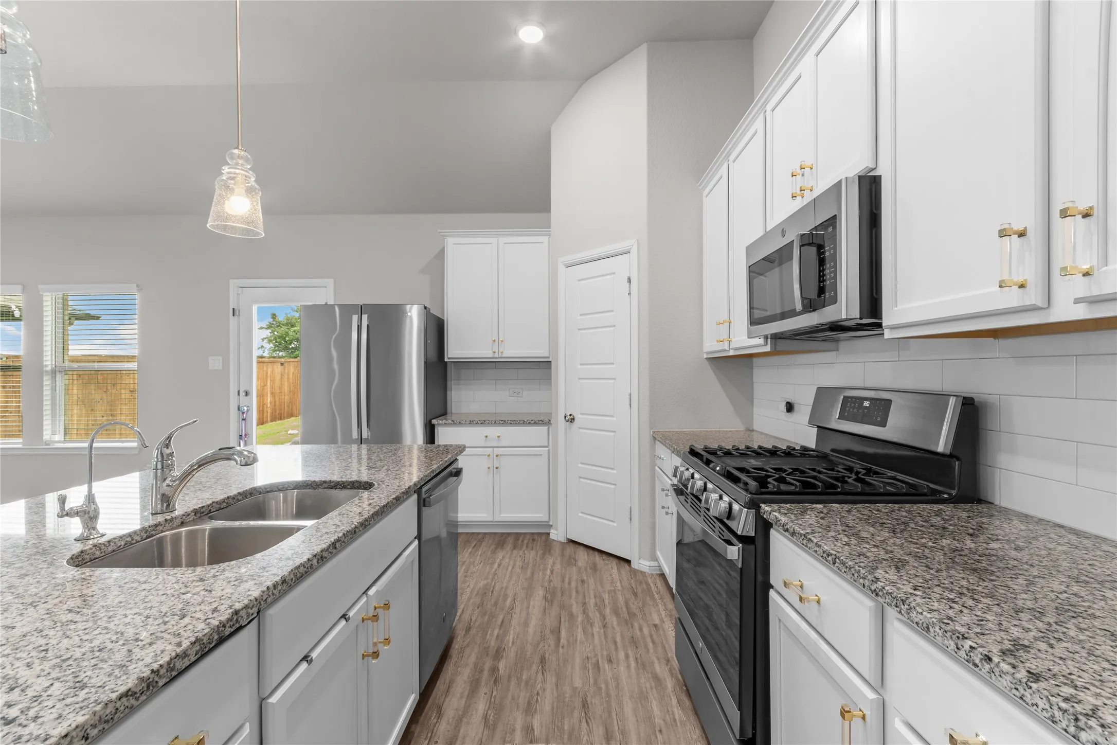 Kitchen featuring an island with a double basin sink, stainless steel appliances, white cabinetry, and granite countertops