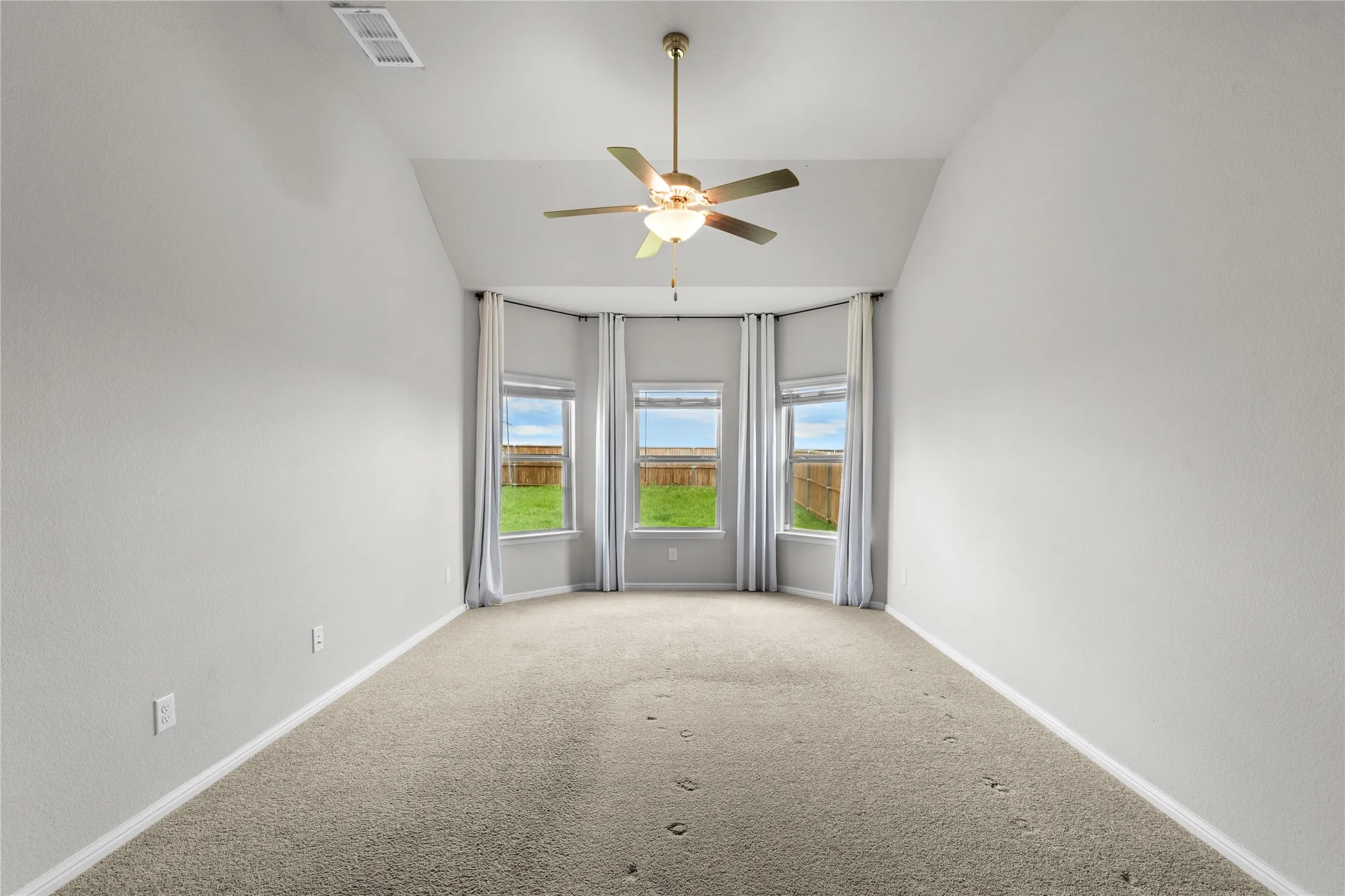 Room featuring a bay window with three individual windows, a ceiling fan with integrated lighting, and vaulted ceilings