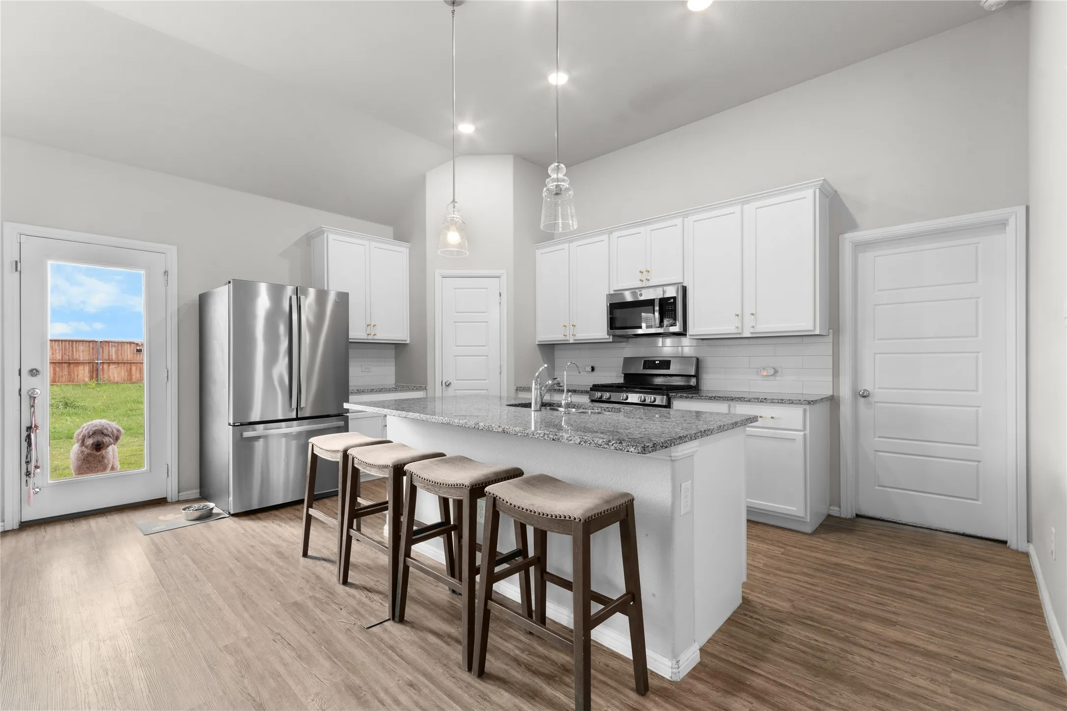 Contemporary kitchen featuring an island with granite countertop, stainless steel appliances, white cabinetry, and wood-finish flooring