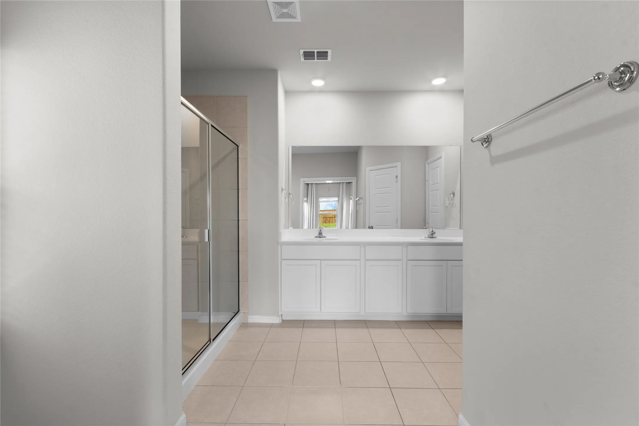 Bathroom featuring a dual vanity with white cabinetry, a large mirrored wall, and a glass-enclosed shower