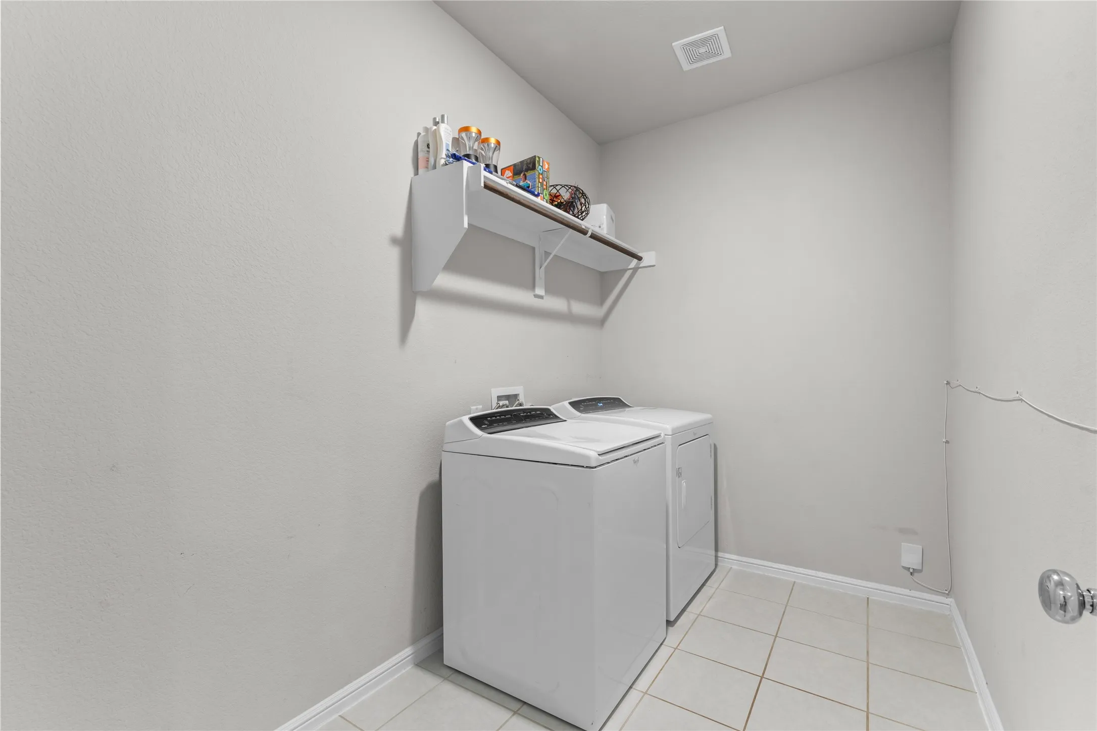 Dedicated utility area featuring a built-in shelving unit, overhead clothes rod, light gray wall paint, white baseboards, and square tile flooring