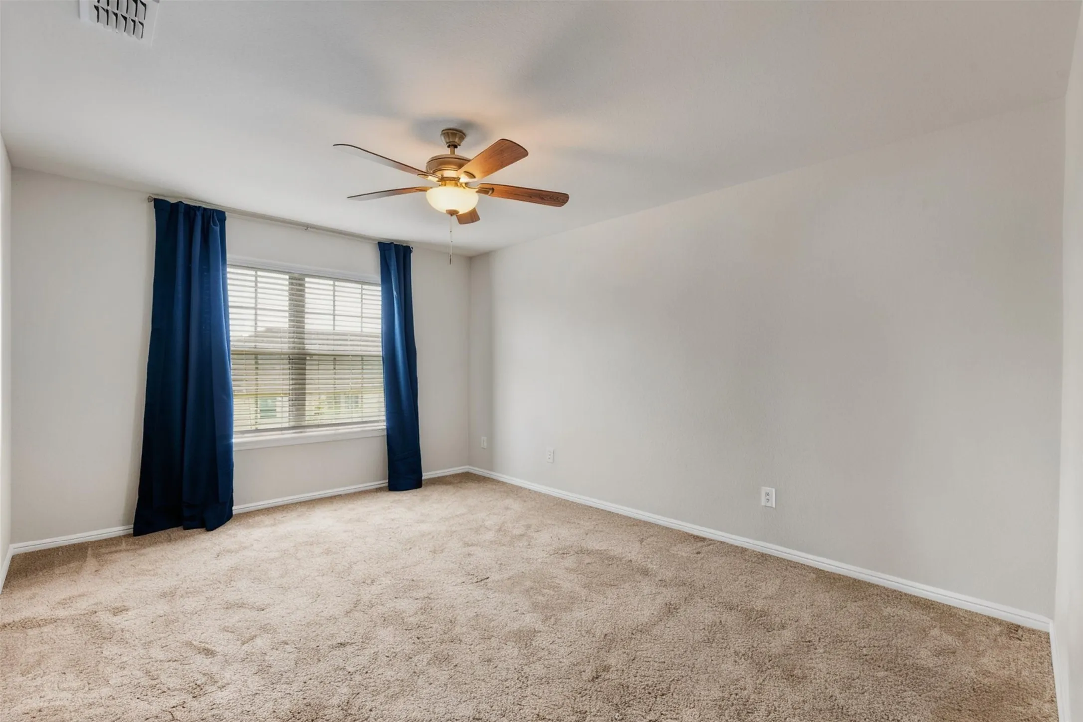 Carpeted room featuring a large window with blinds, a ceiling fan with light fixture, and light-toned walls