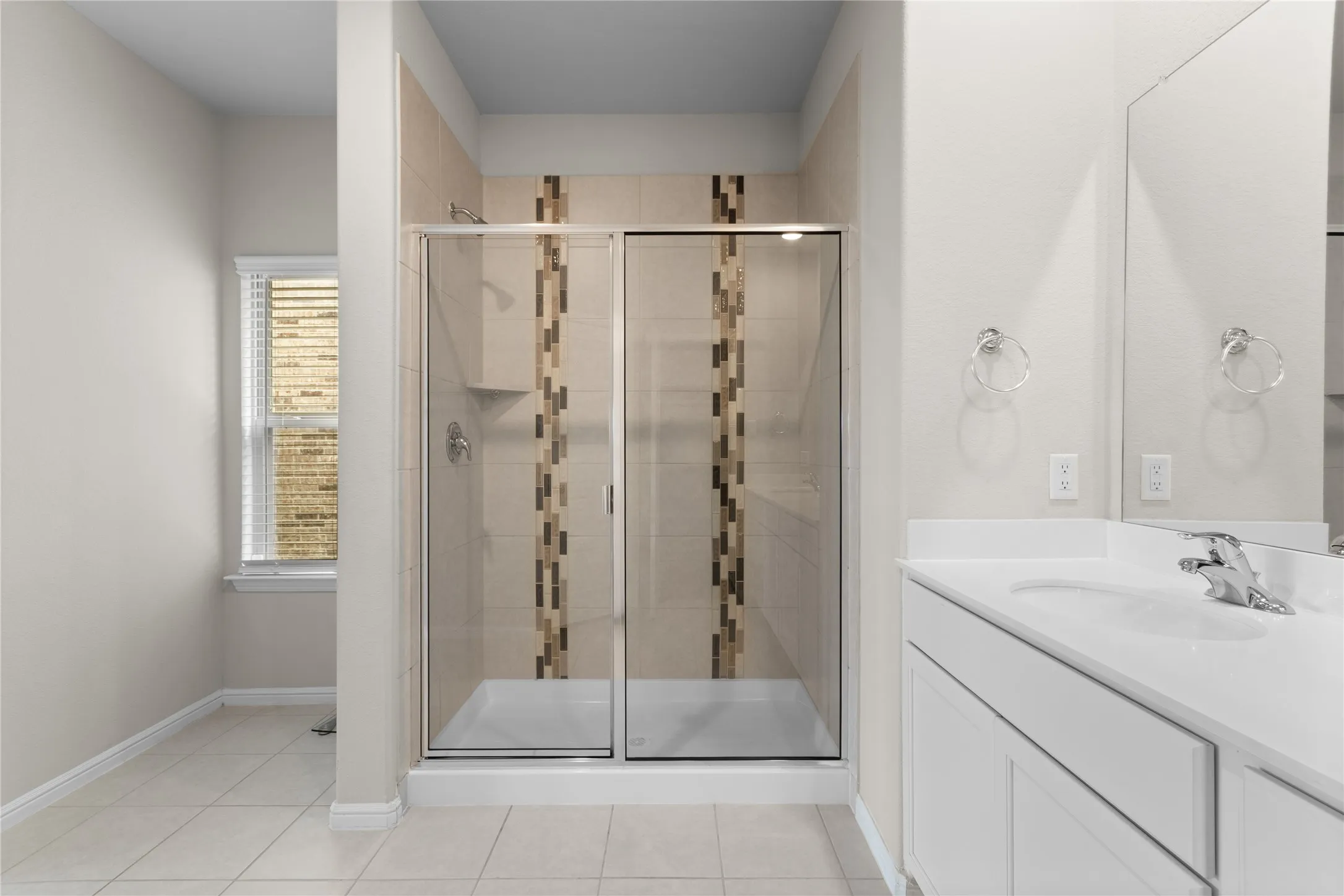 Shower enclosure with glass doors and accent tile, single vanity with integrated sink, chrome faucet, and mirrored wall
