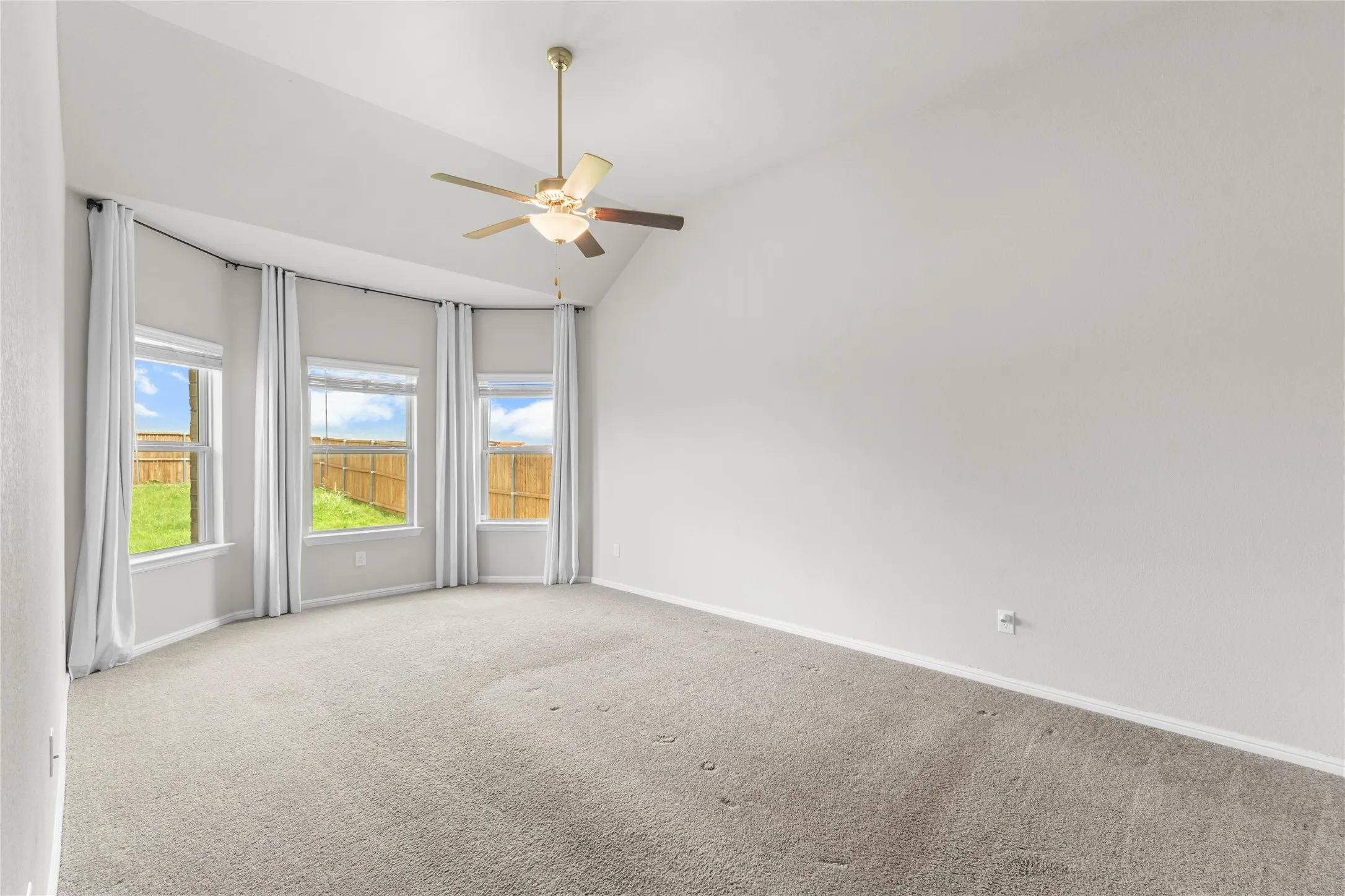 Spacious room featuring a vaulted ceiling with a brass-finish ceiling fan, neutral carpet, and a bay window with three double-hung windows