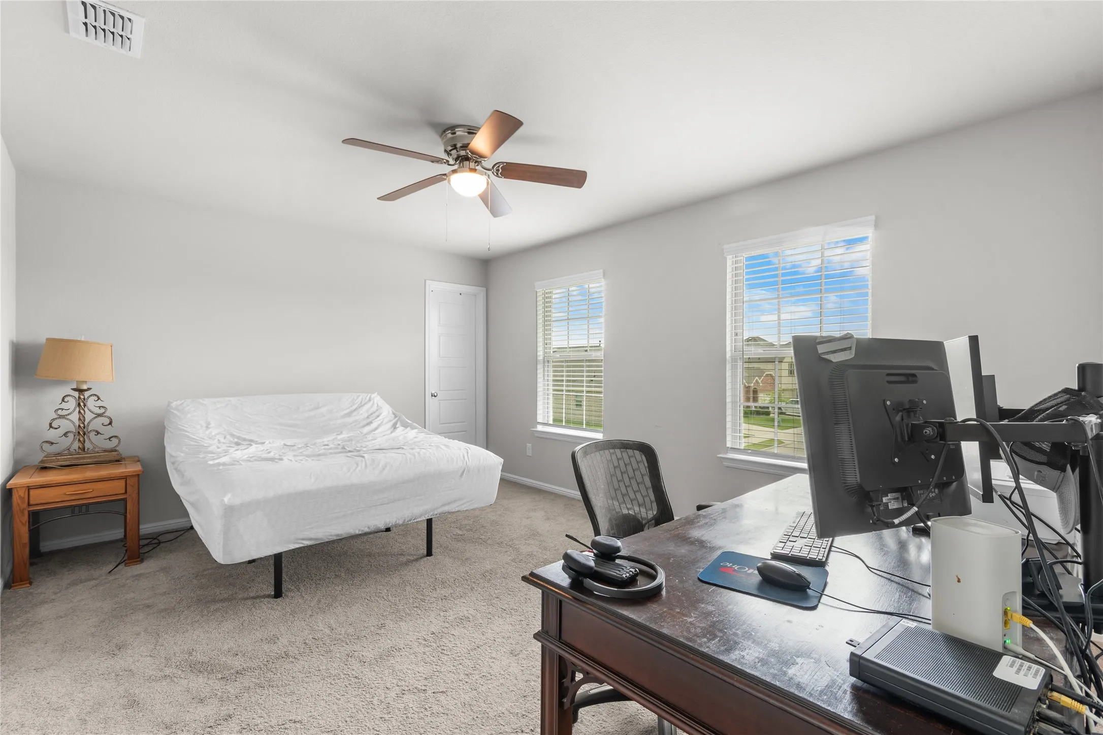 Spacious room featuring neutral paint, gray carpet flooring, two windows with blinds, and a ceiling fan with integrated lighting