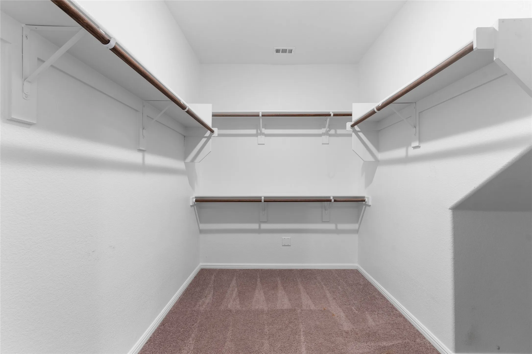 Walk-in closet with carpet flooring, white walls, and multiple wood-finish hanging rods