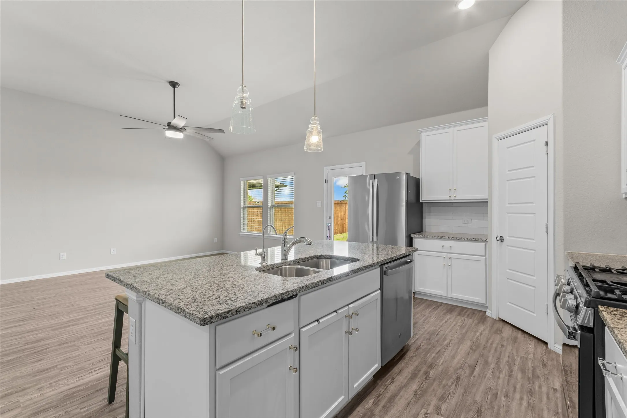 Kitchen island with a double basin sink, stainless steel appliances, white cabinetry, wood-finish flooring, and vaulted ceiling
