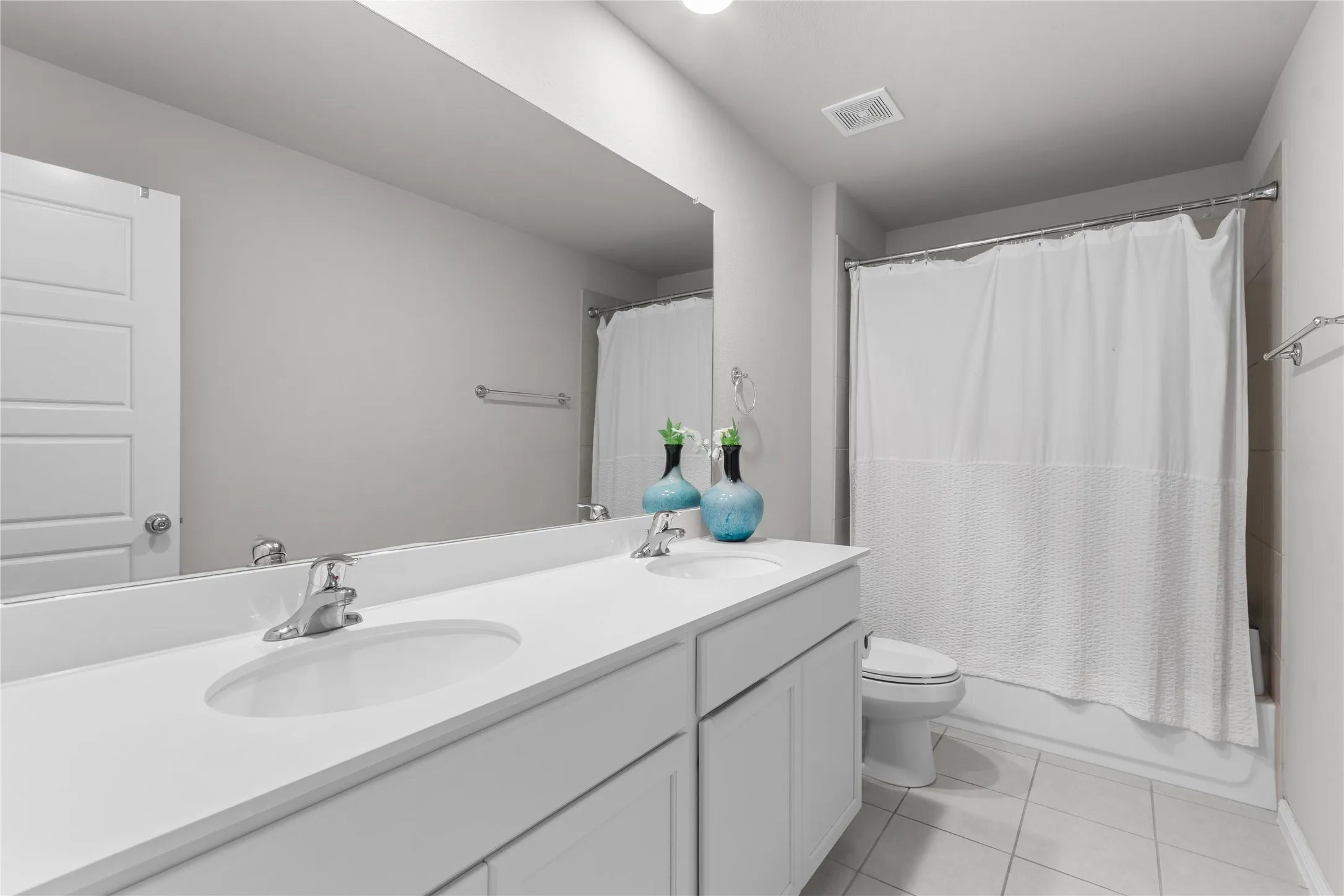 Bathroom featuring a dual-sink vanity with a white countertop, chrome fixtures, and a large wall-mounted mirror