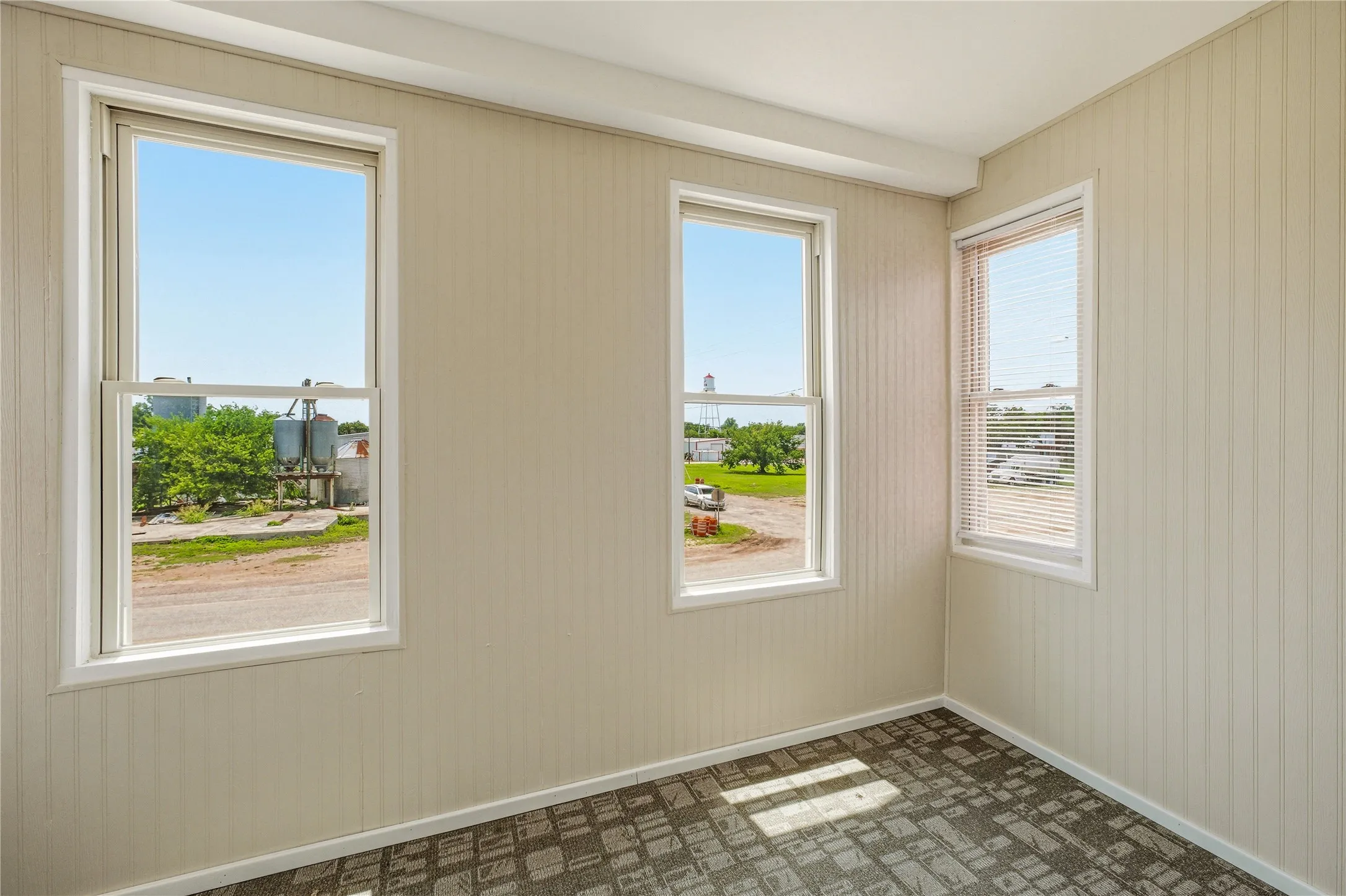 Room featuring three windows with white trim, beadboard wall paneling, and a textured carpeted floor