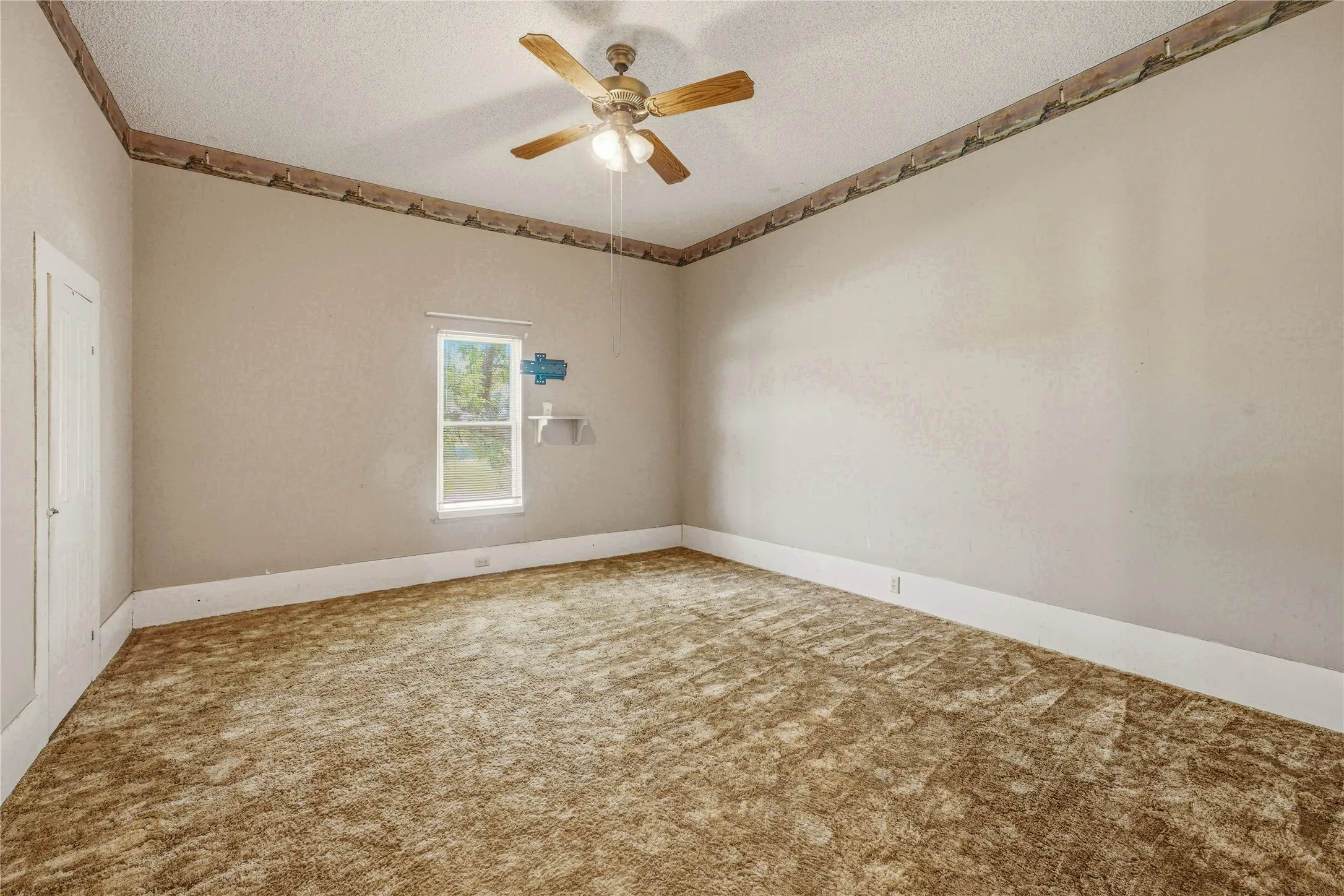 Spacious room featuring textured walls, a single window, and a built-in shelf