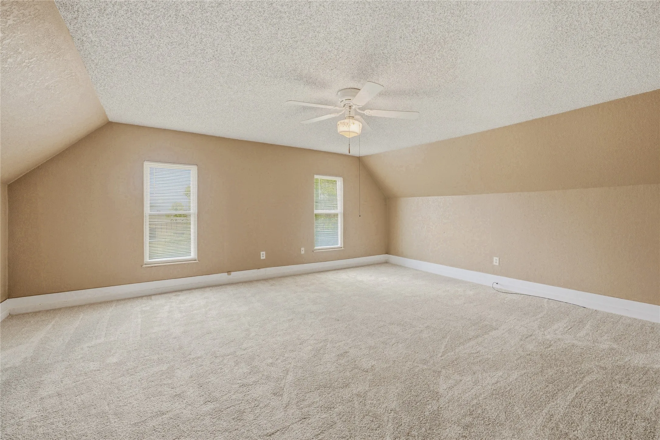 Spacious room featuring vaulted ceilings, two windows, wall-to-wall carpeting, and a ceiling fan with integrated lighting