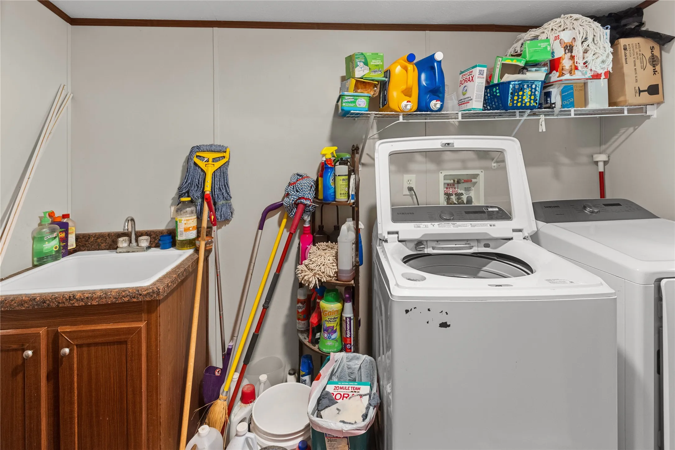 Dedicated laundry area featuring a utility sink with a laminate countertop, built-in cabinetry, wall-mounted shelving, and appliance hookups