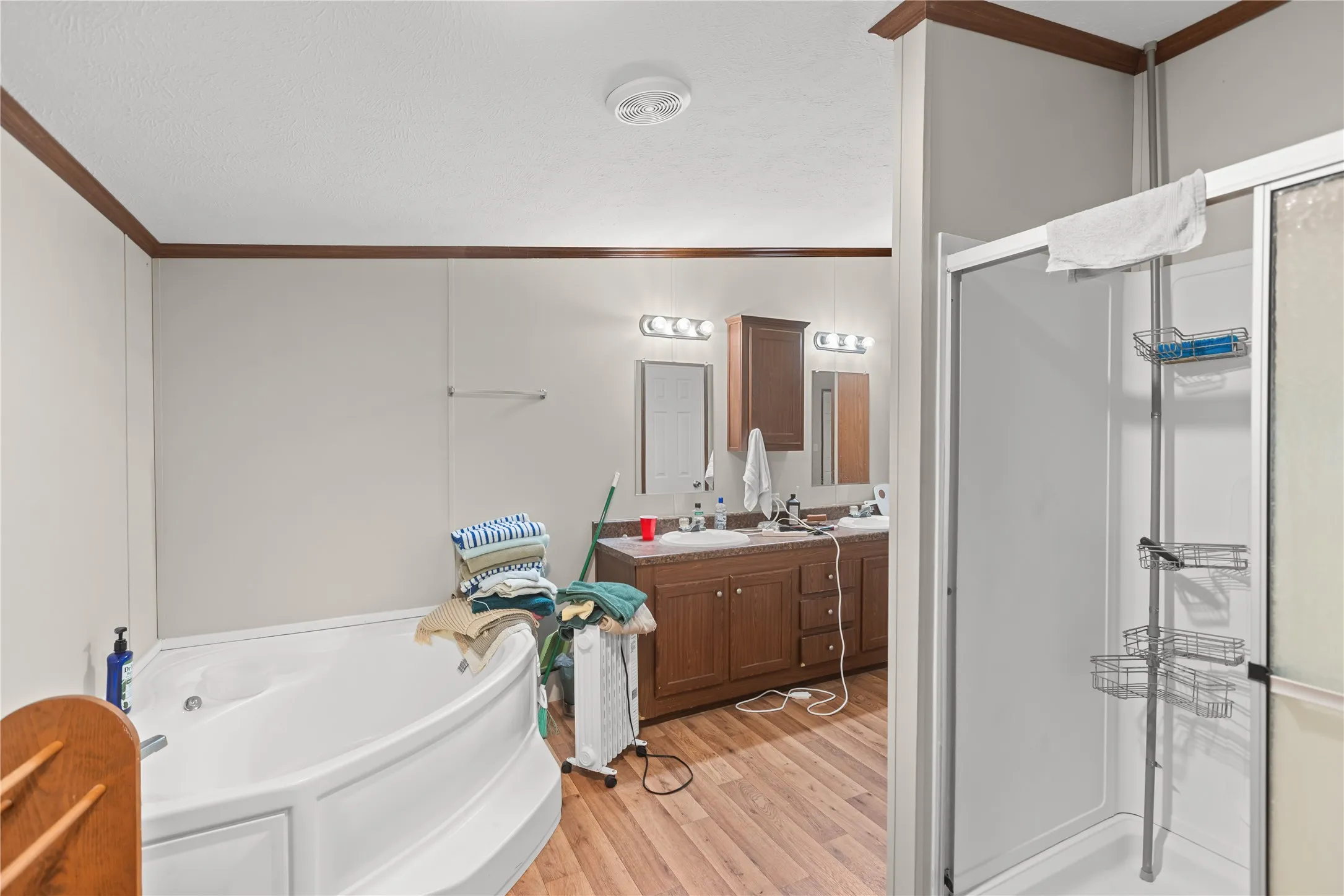 Bathroom featuring a corner soaking tub, wood-finish flooring, and a dual vanity with a dark wood cabinet and white countertops