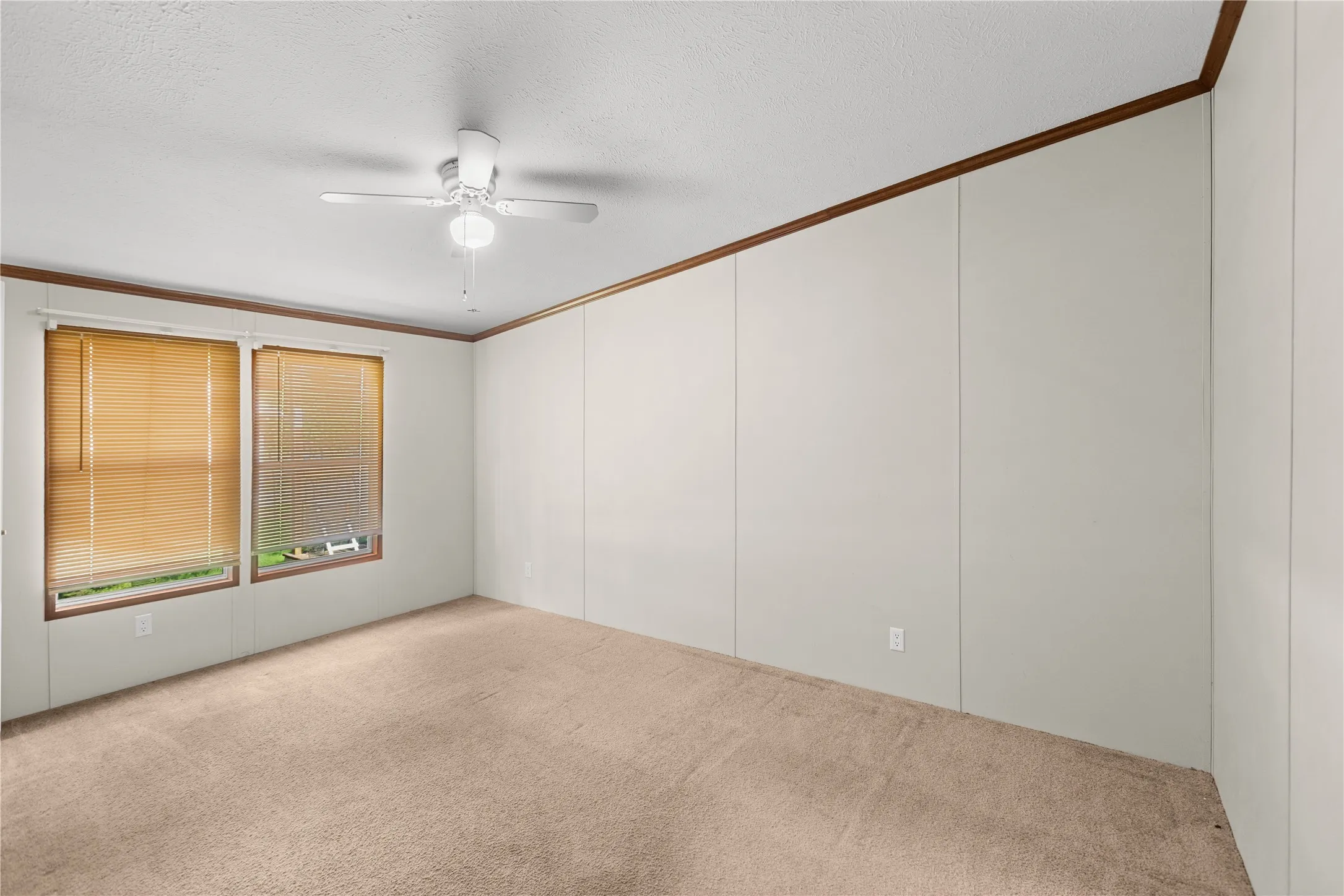 Carpeted room featuring two windows with horizontal blinds, a ceiling fan with integrated lighting, and wood-trim accents