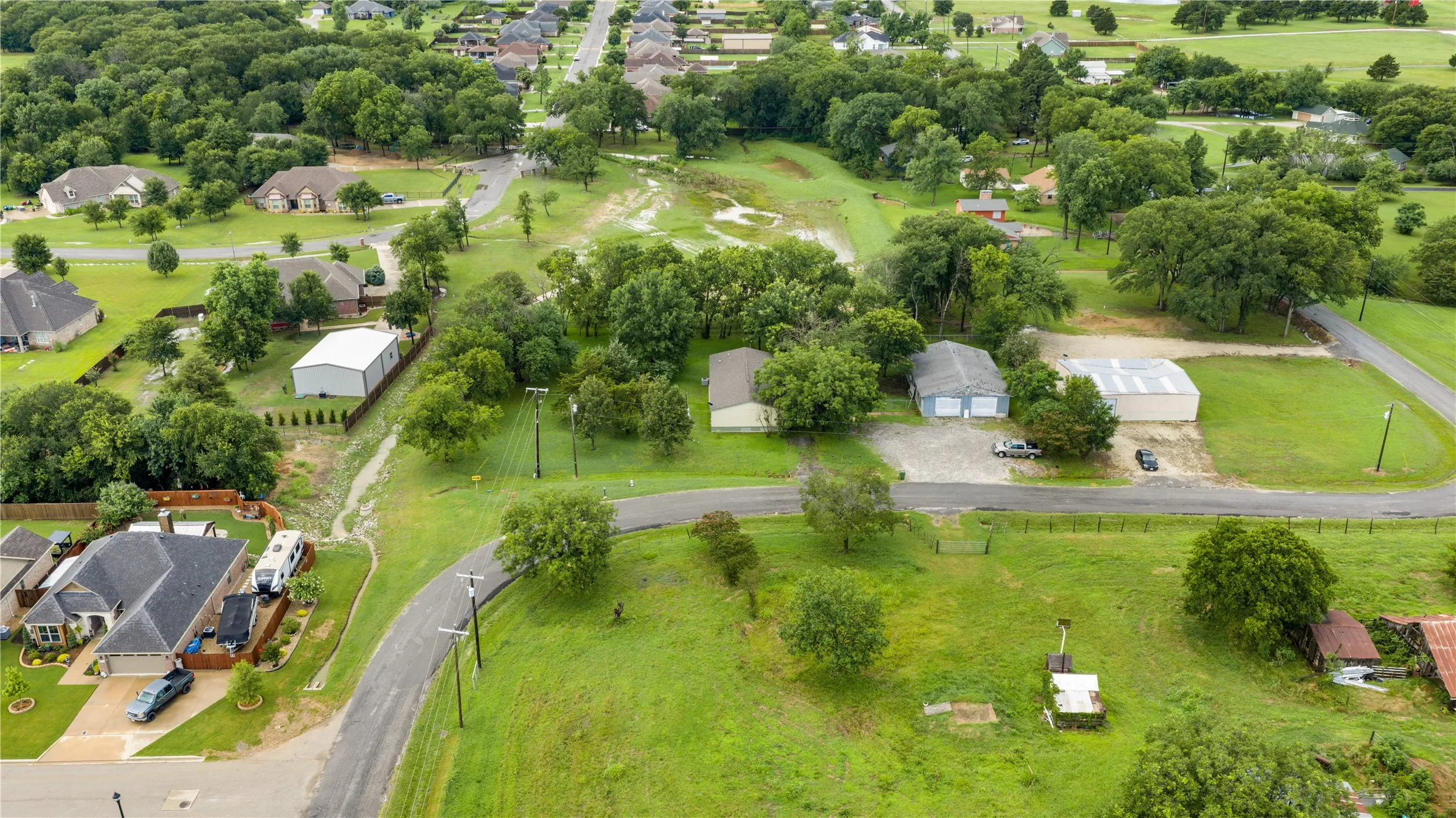 Expansive property featuring multiple structures, including a primary residence with a dark shingle roof, two detached garage buildings, and a large metal outbuilding