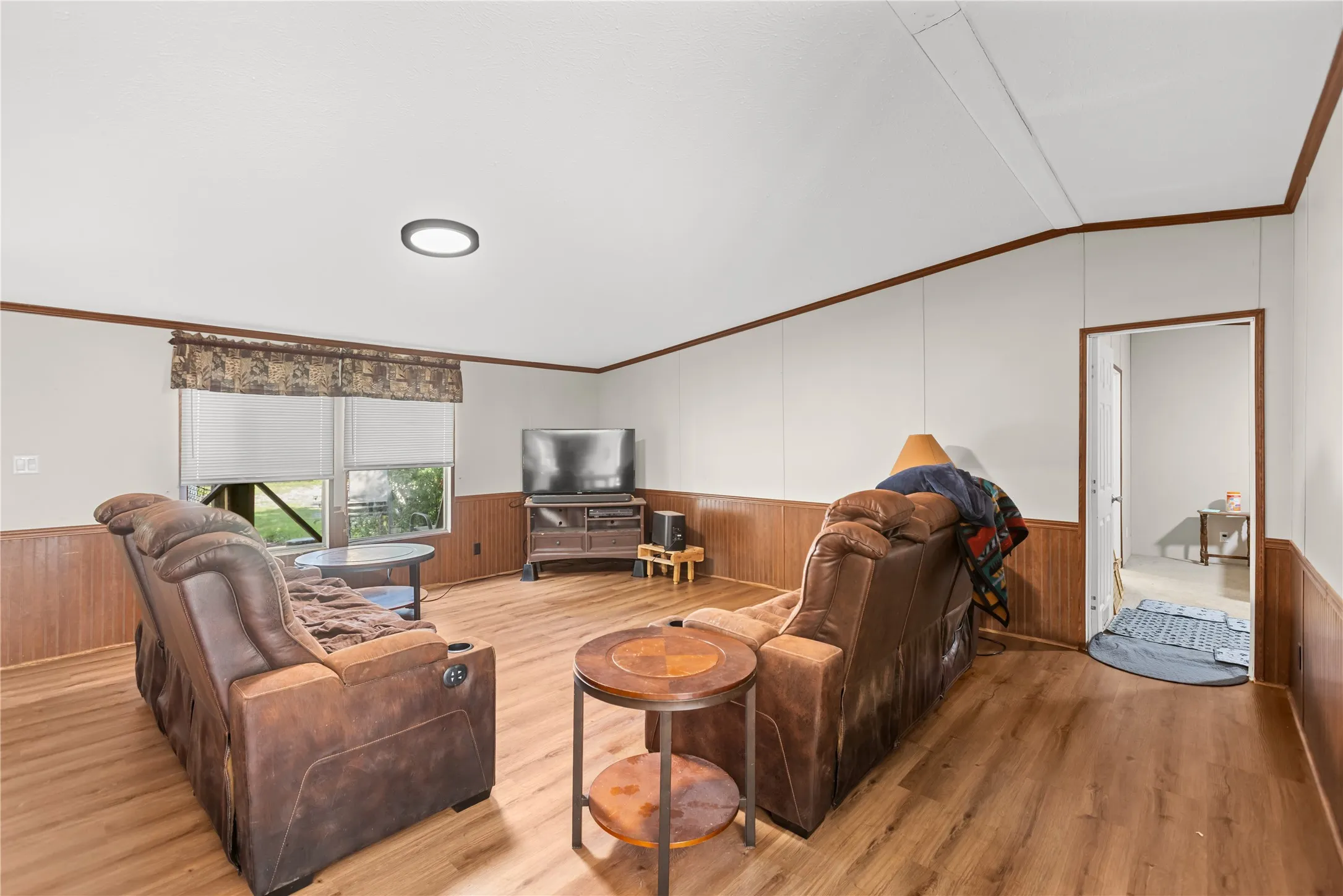Expansive living area featuring wood-finish flooring, half-wall wainscoting, white panel walls, and a flush-mount ceiling light fixture