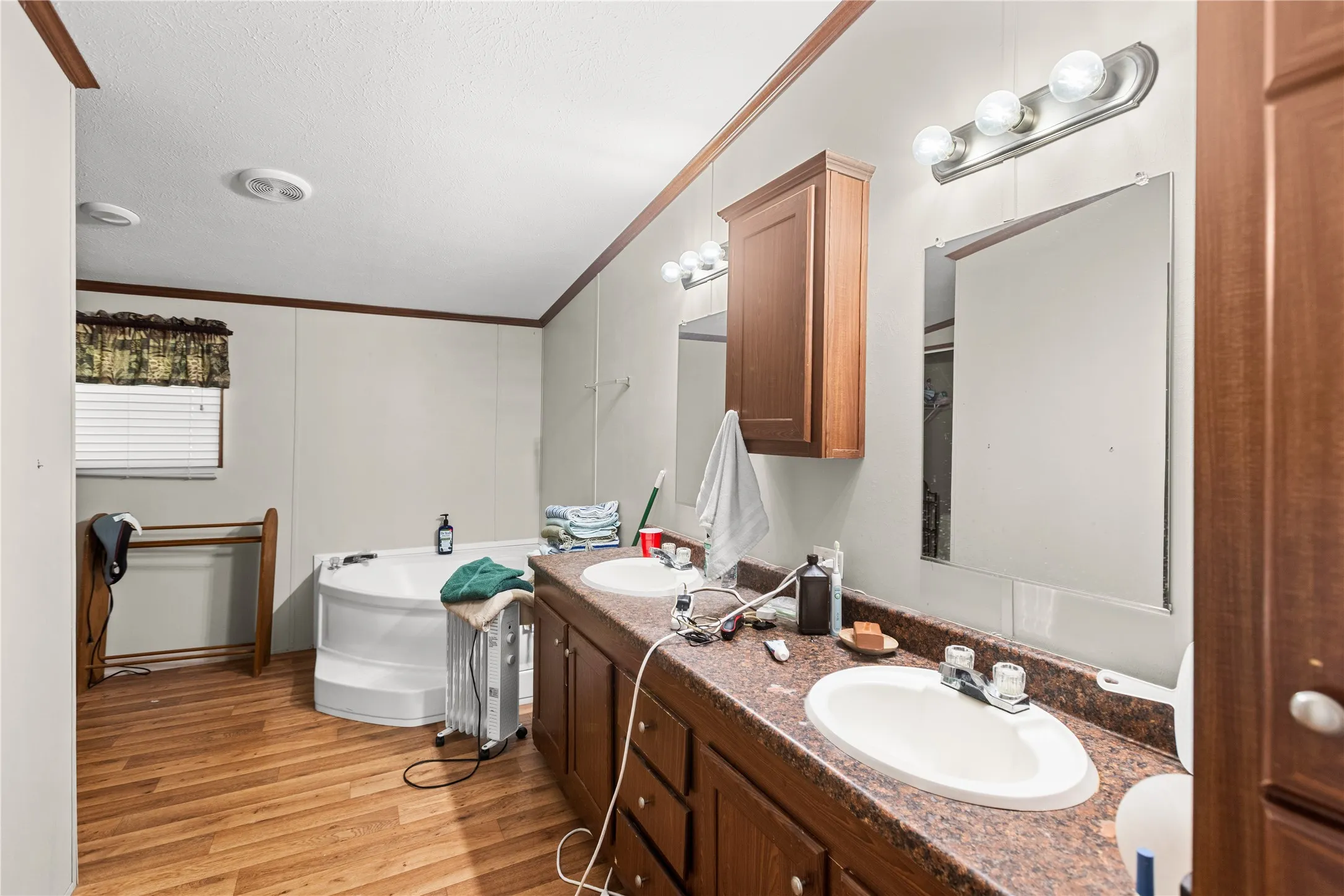 Bathroom featuring a corner soaking tub, wood-finish flooring, dual vanity with undermount sinks, and wall-mounted mirrors