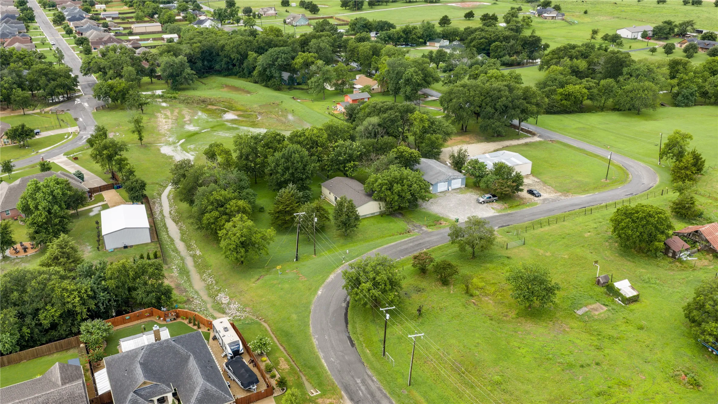 Expansive landscape featuring large parcels of land, mature trees, and a winding paved road