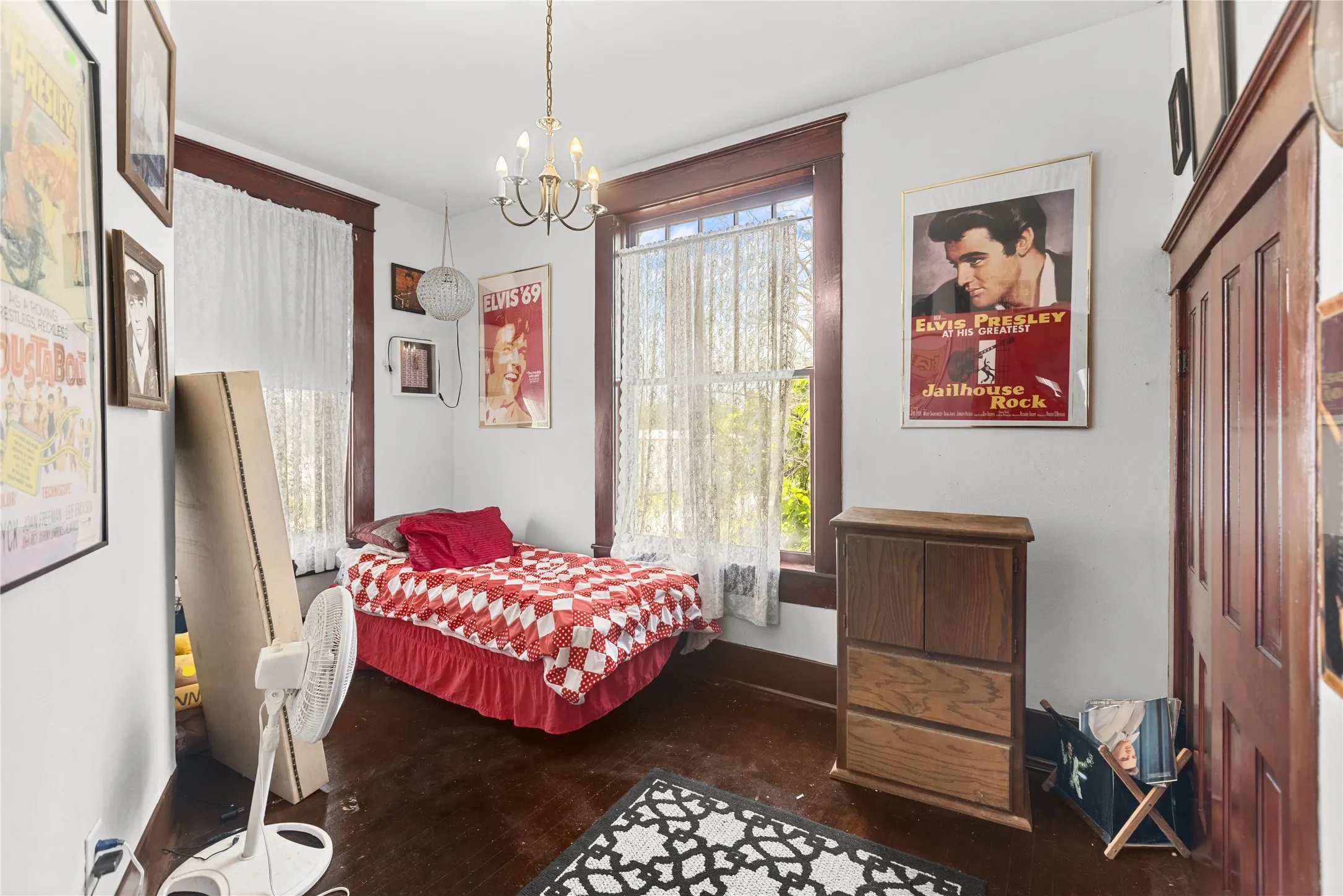 Room featuring two windows with white lace curtains, dark wood-finish flooring, and a brass chandelier