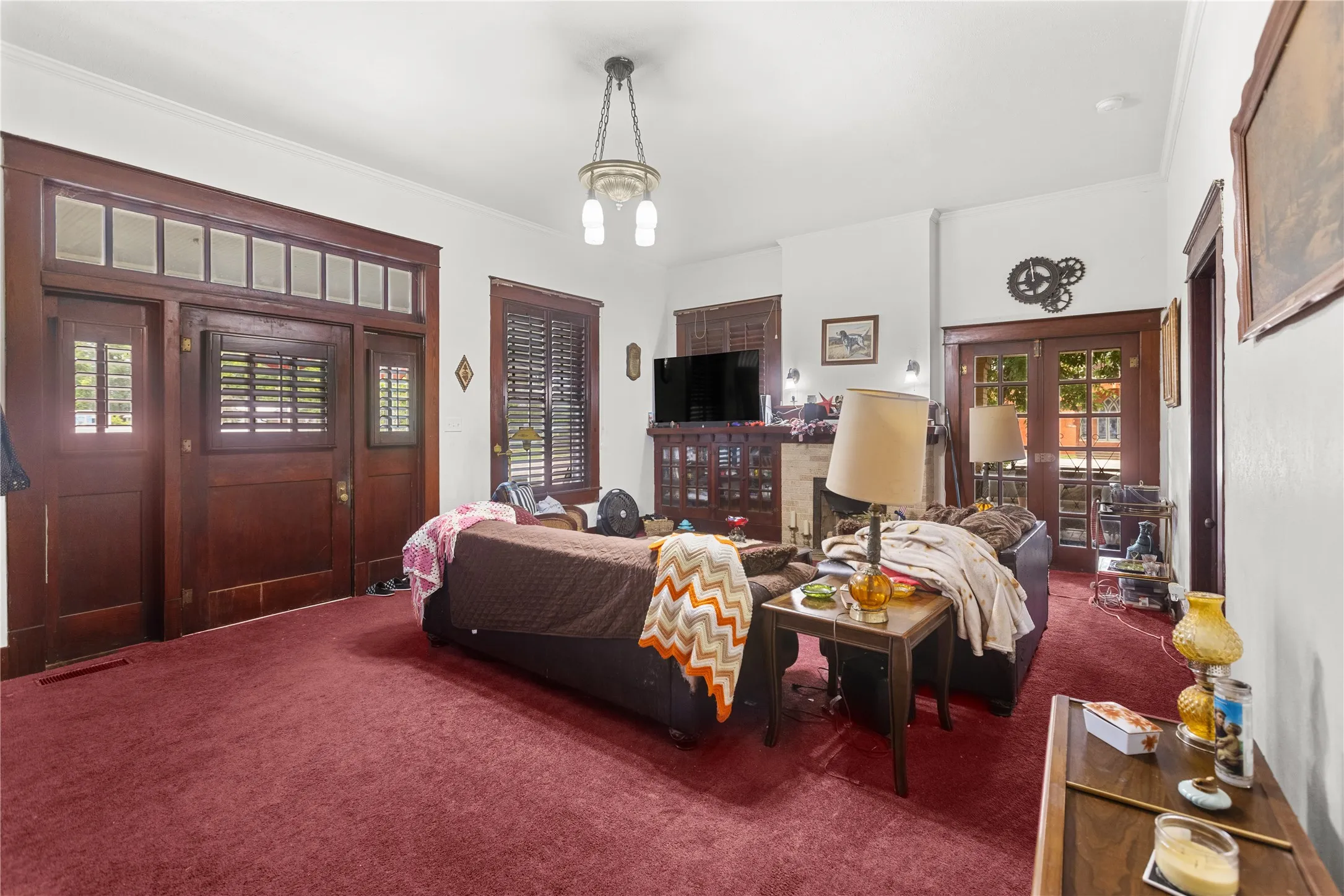 Living space featuring rich wood-finish trim and doors, red carpeting, a central chandelier, and white wall finishes