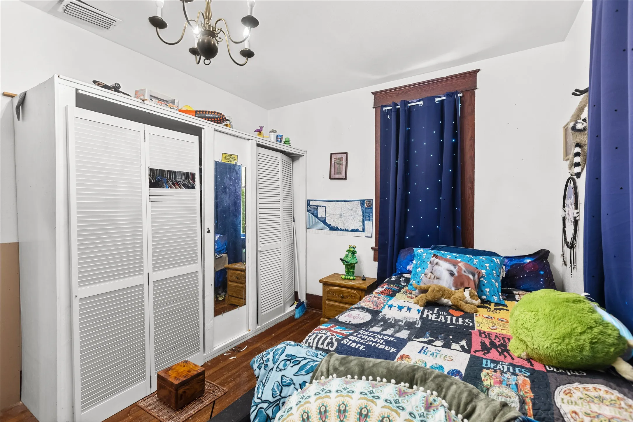 Bedroom featuring wood-finish flooring, a decorative chandelier, and a window with dark wood trim
