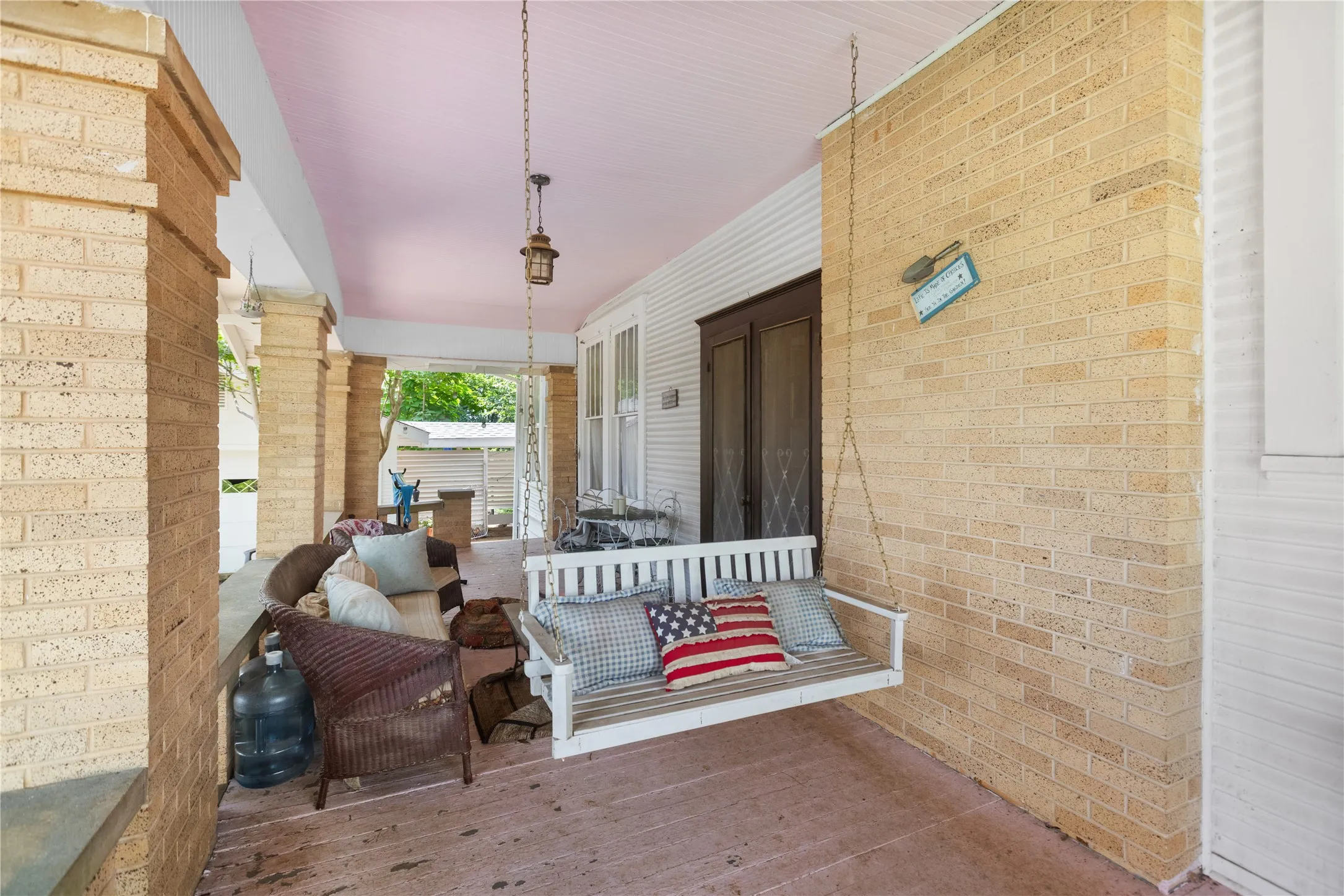 Covered porch featuring a porch swing, beadboard ceiling, and brick columns