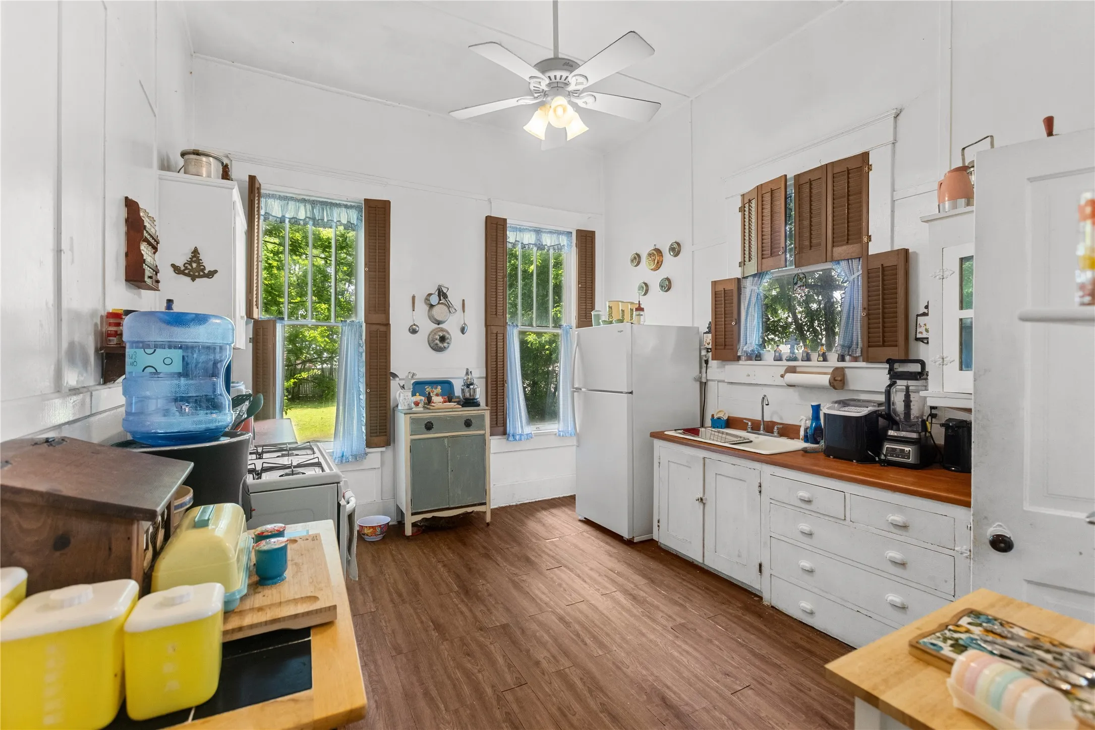 Kitchen featuring wood-finish flooring, white cabinetry, a built-in sink, and multiple windows with shutter accents