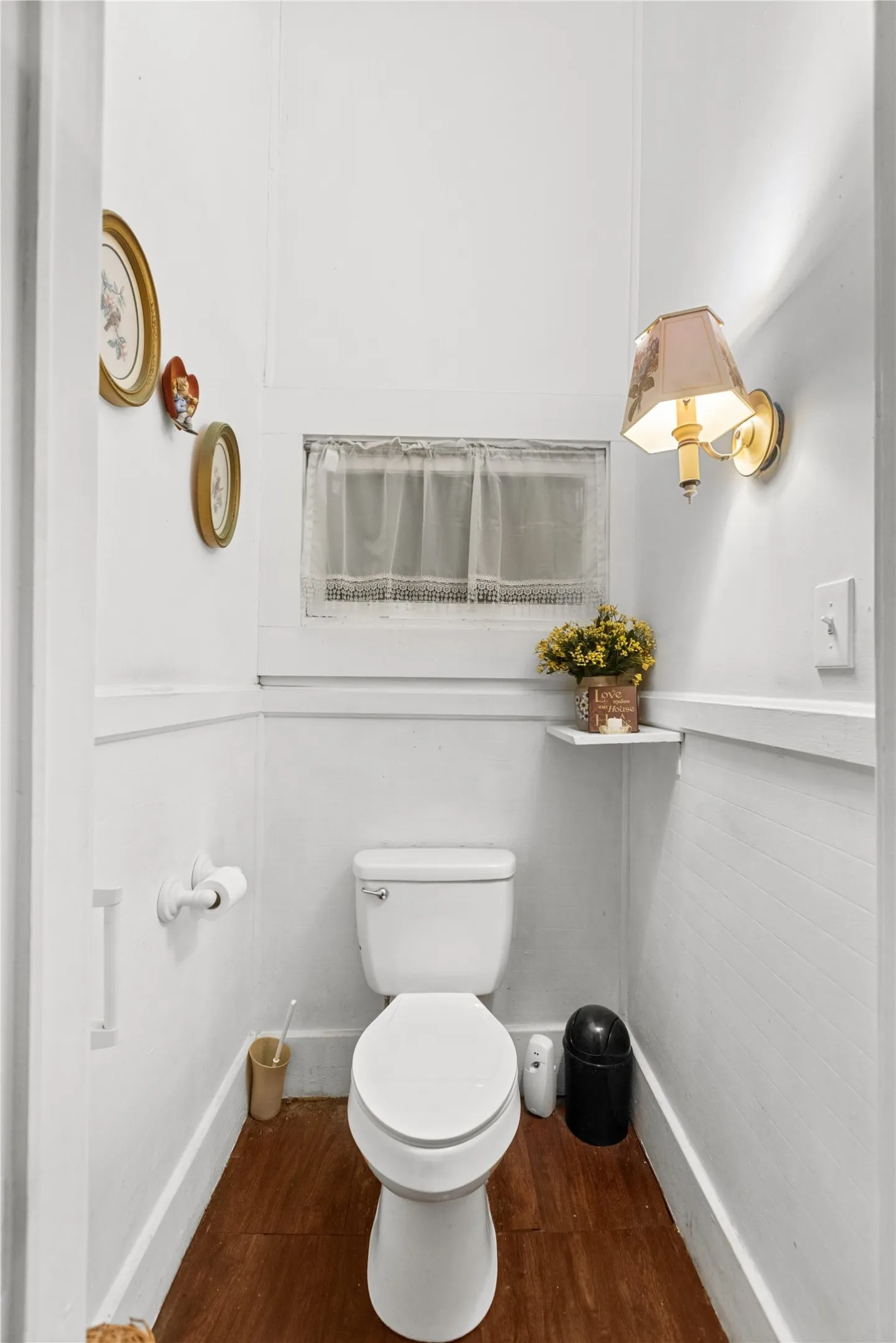 Compact powder room featuring a white toilet, wood-finish flooring, and a wall-mounted sconce