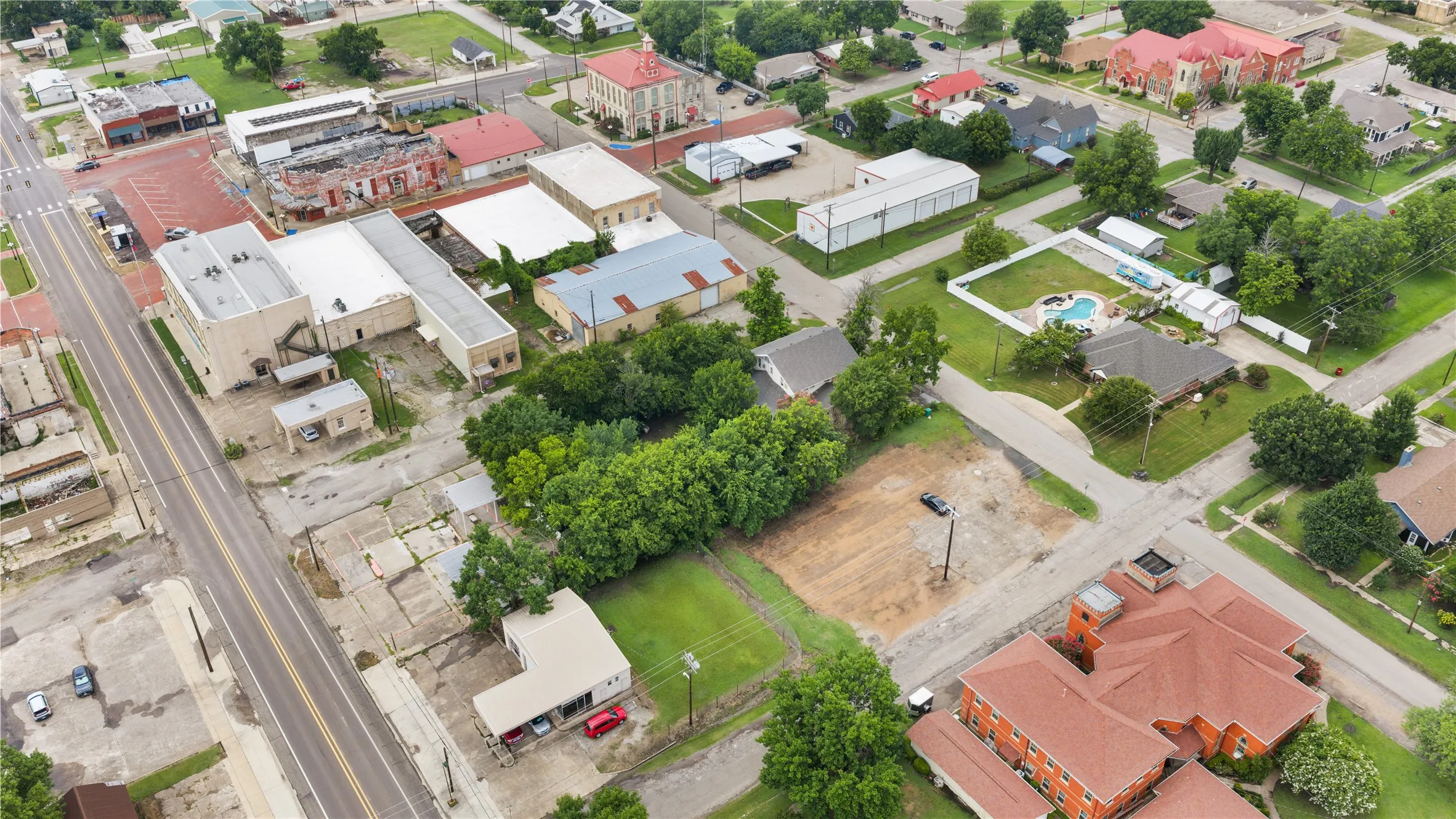 Aerial perspective showcasing a mixed-use neighborhood with commercial buildings, residential properties, and undeveloped land parcels
