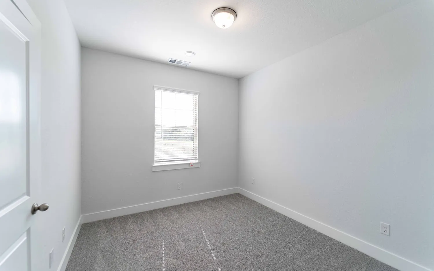 Carpeted room featuring a single window with blinds, a white paneled door, and a flush-mount ceiling light