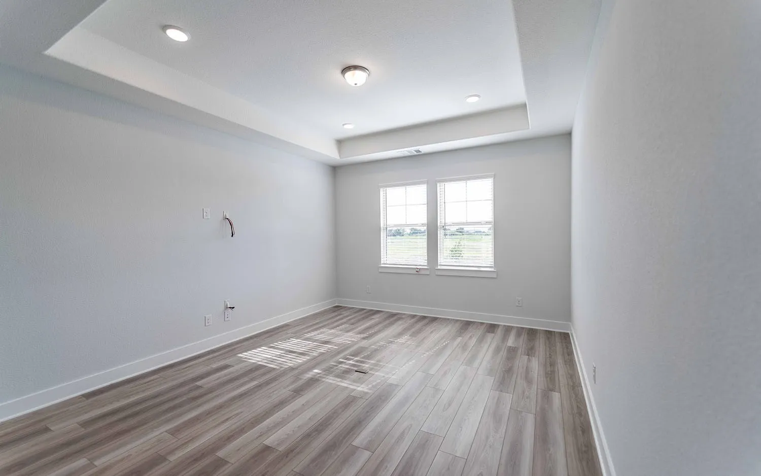 Recessed lighting illuminating a tray ceiling, wood-finish flooring, and white trim throughout