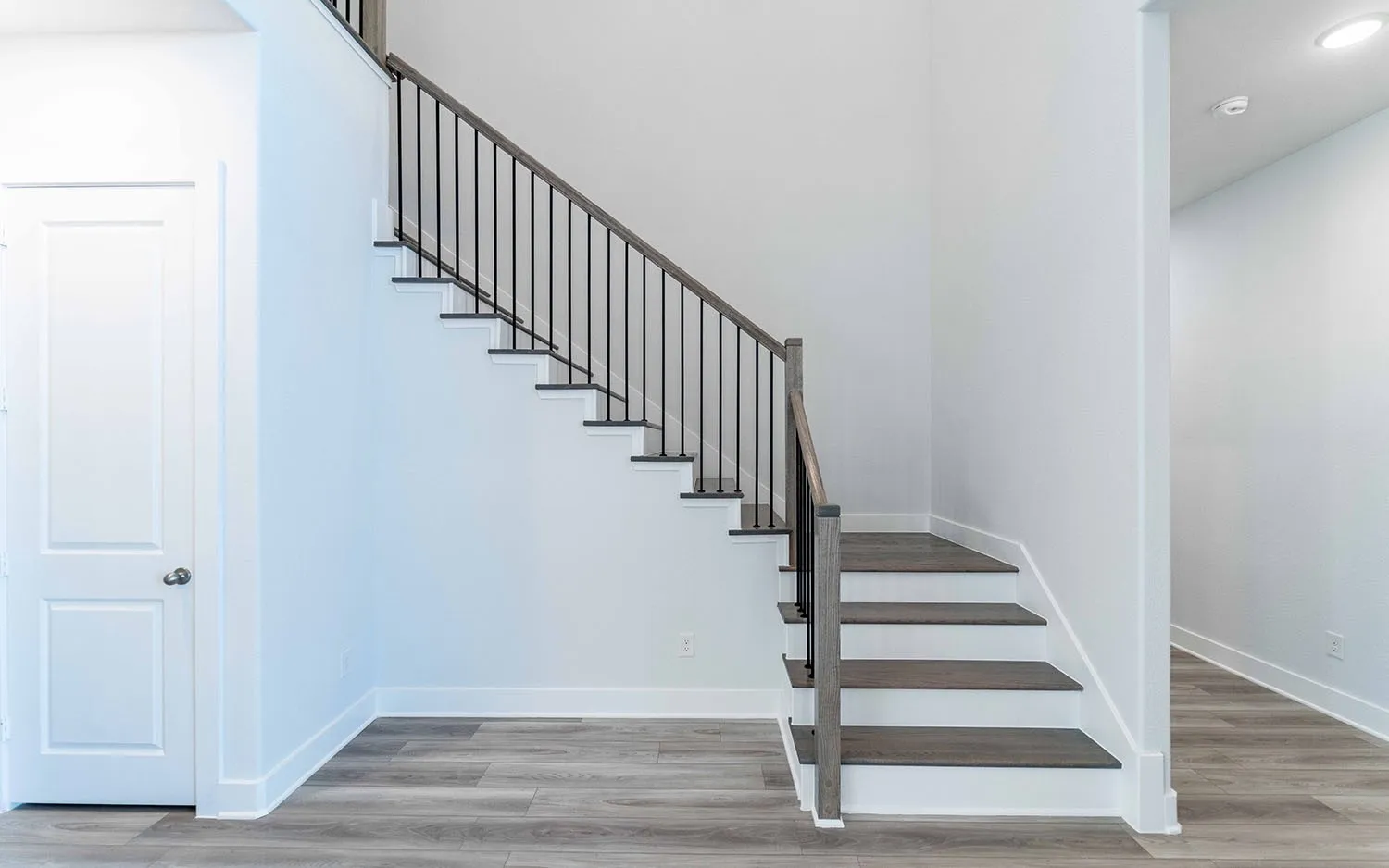 Contemporary staircase featuring dark wood-finish treads, white risers, and a black wrought iron baluster system