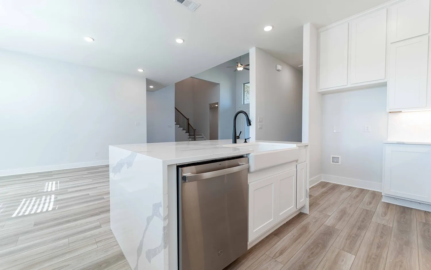 Kitchen island featuring a farmhouse sink, matte black faucet, and integrated stainless steel dishwasher