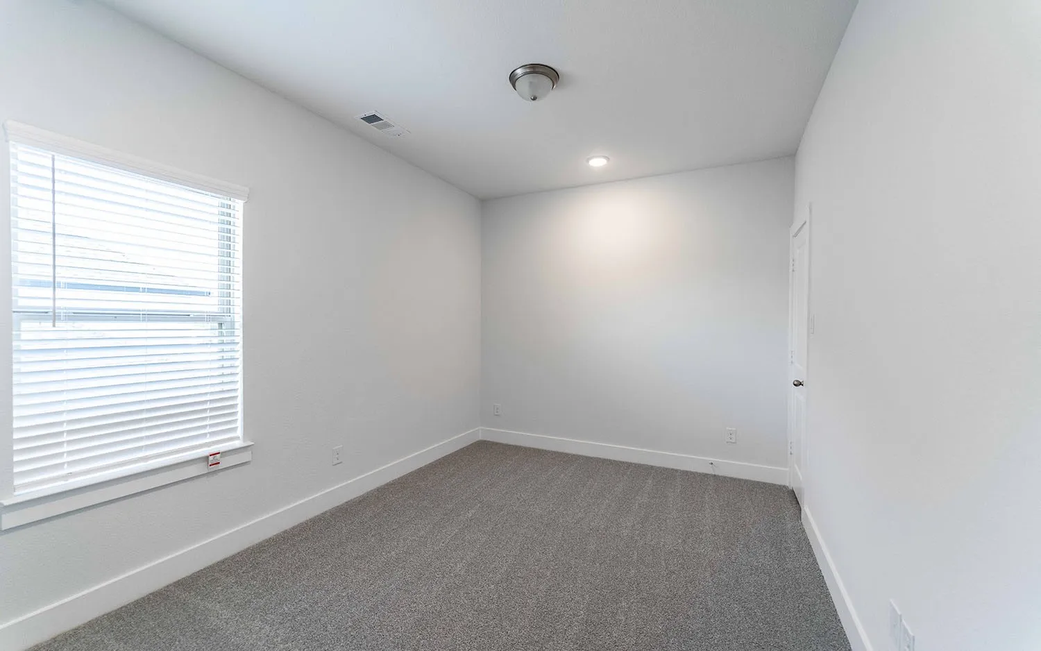 Carpeted room featuring a window with blinds, white trim, a flush mount light fixture, and an additional recessed light