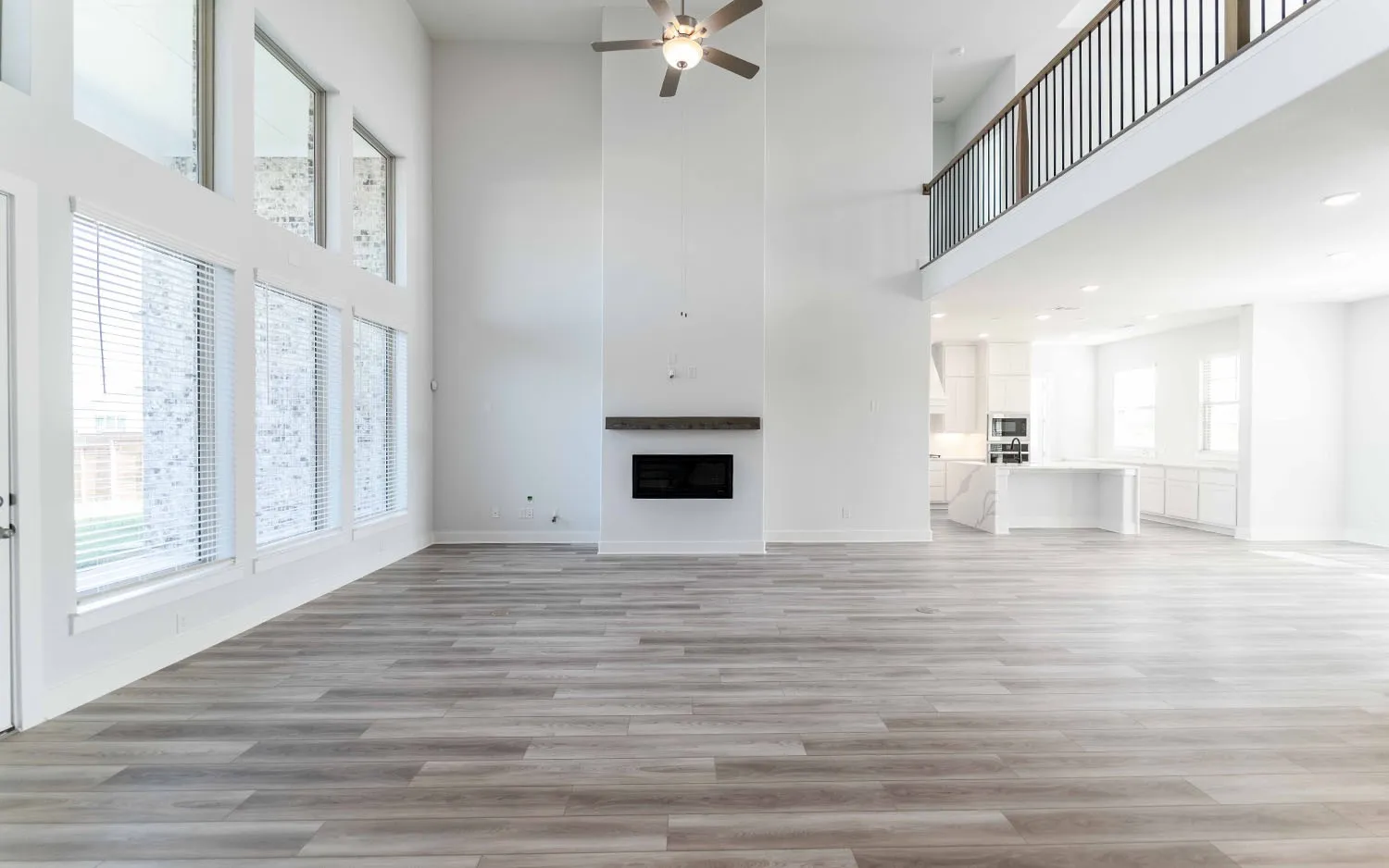 Two-story living area featuring wood-finish flooring, a contemporary fireplace with a floating mantel, and a ceiling fan