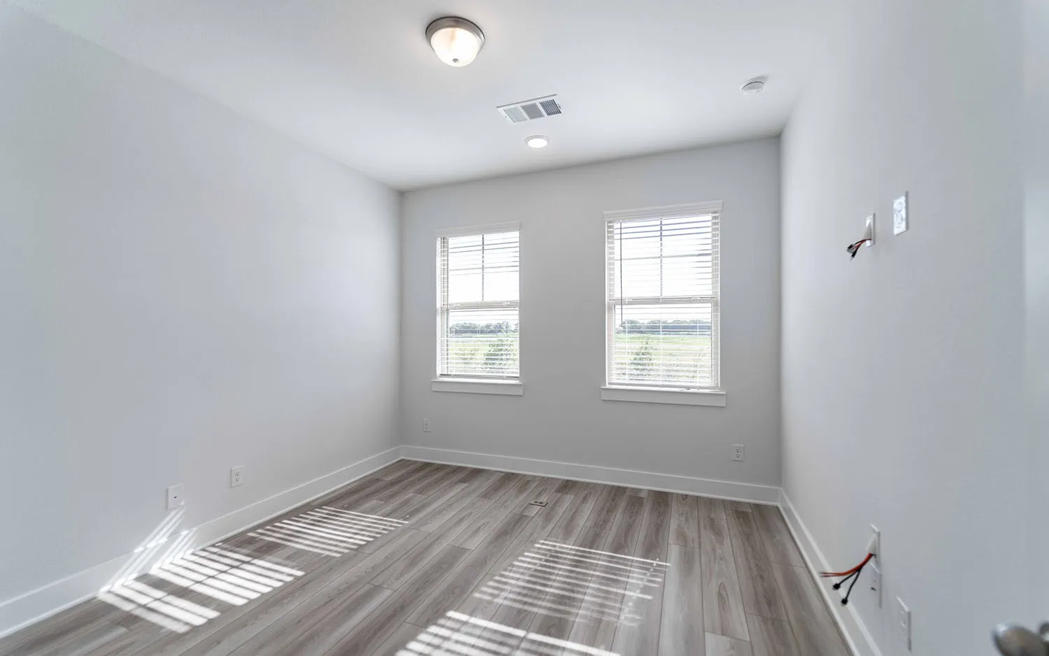 Neutral-toned room with wood-finish flooring, two windows with blinds, and white baseboards