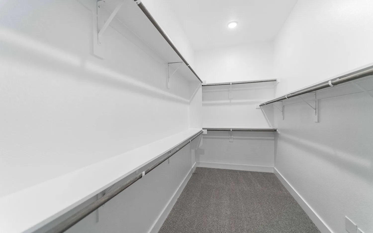 Walk-in closet featuring white painted walls, multiple white shelving units, metal hanging rods, recessed ceiling lighting, and gray carpet flooring