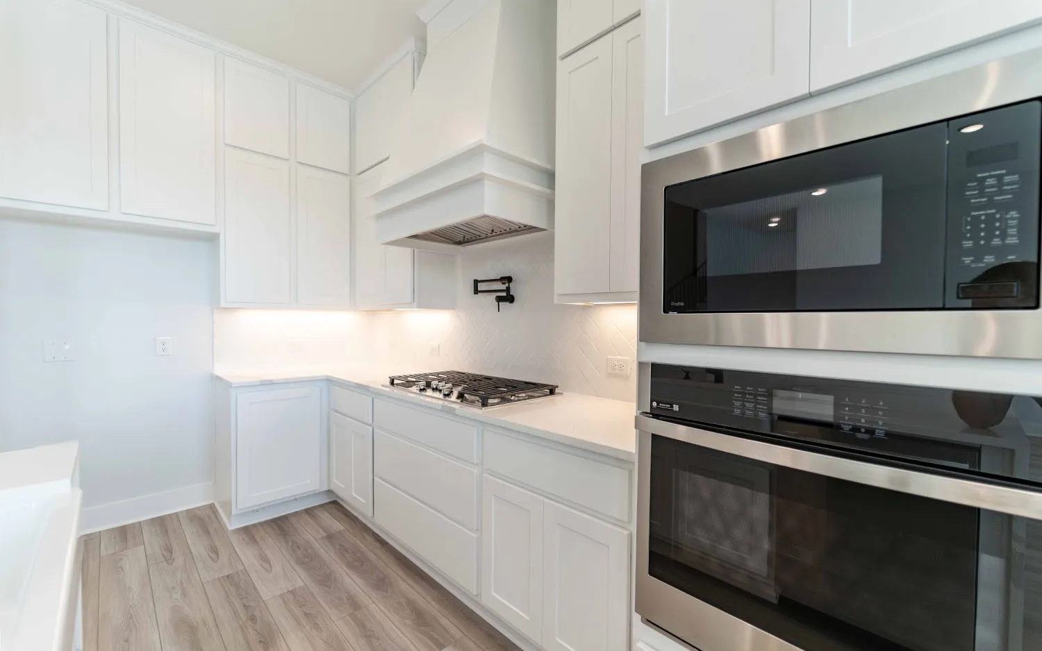 Bright kitchen featuring white shaker cabinetry, stainless steel built-in appliances, a gas cooktop, and light wood-finish flooring